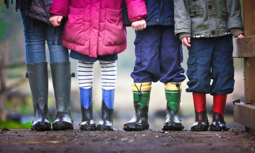 Four children from the waist down dressed in rain coats and rain boors