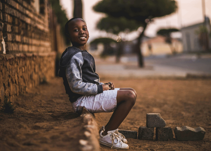 Young boy sitting on curb smiling at the camera
