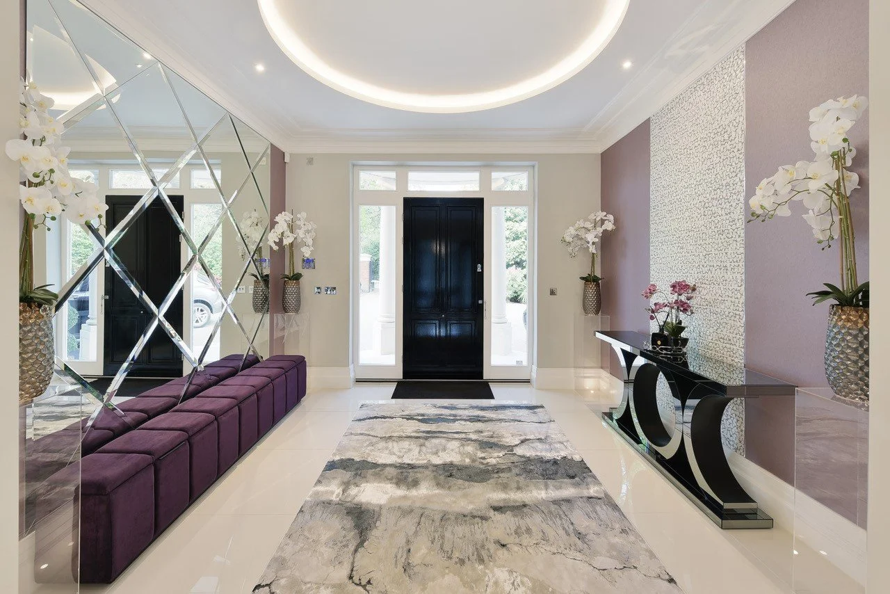 Modern entryway with black front door, marble flooring, upholstered storage velvet bench, decorative mirror wall, and vases with white orchids and pink flowers.