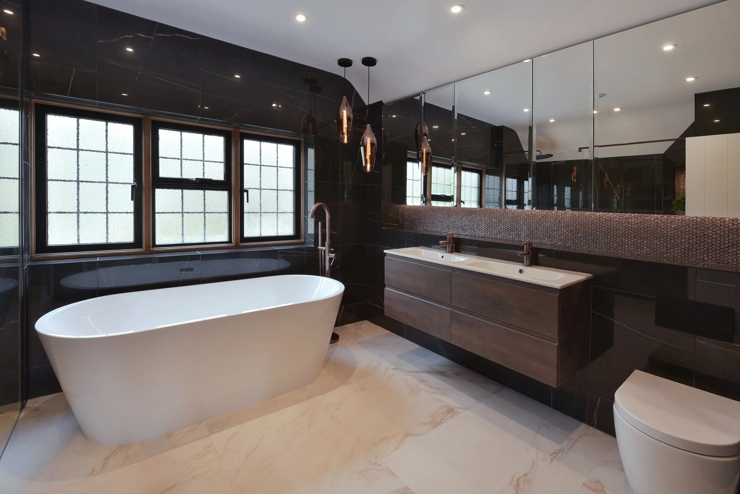 Modern bathroom with a freestanding bathtub, Puntotre Italian double vanity with copper bronze taps, marble tiled walls. Bathroom pendant lights create mood lighting.