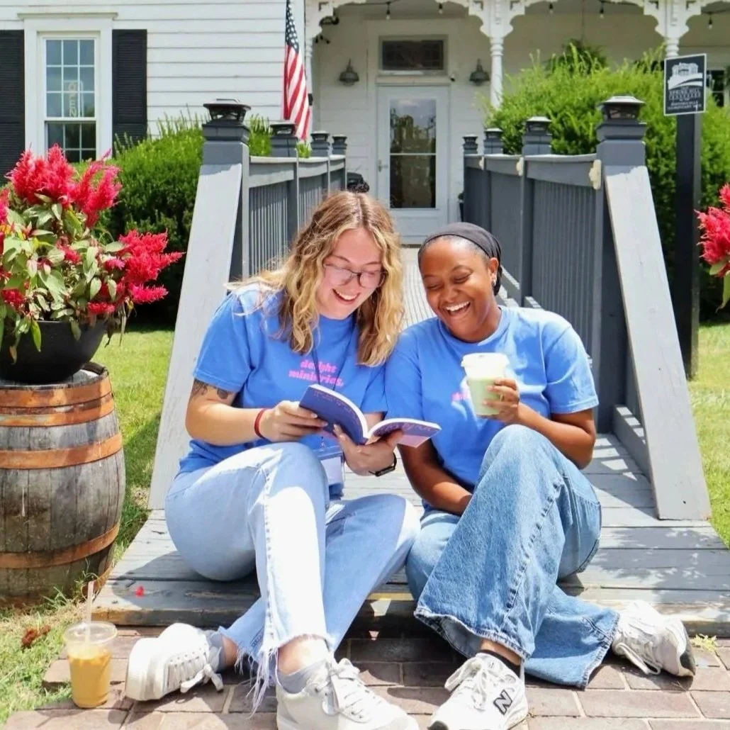2 Delight girls in Delight t-shirts reading a Delight study together in a beautiful yard outside.