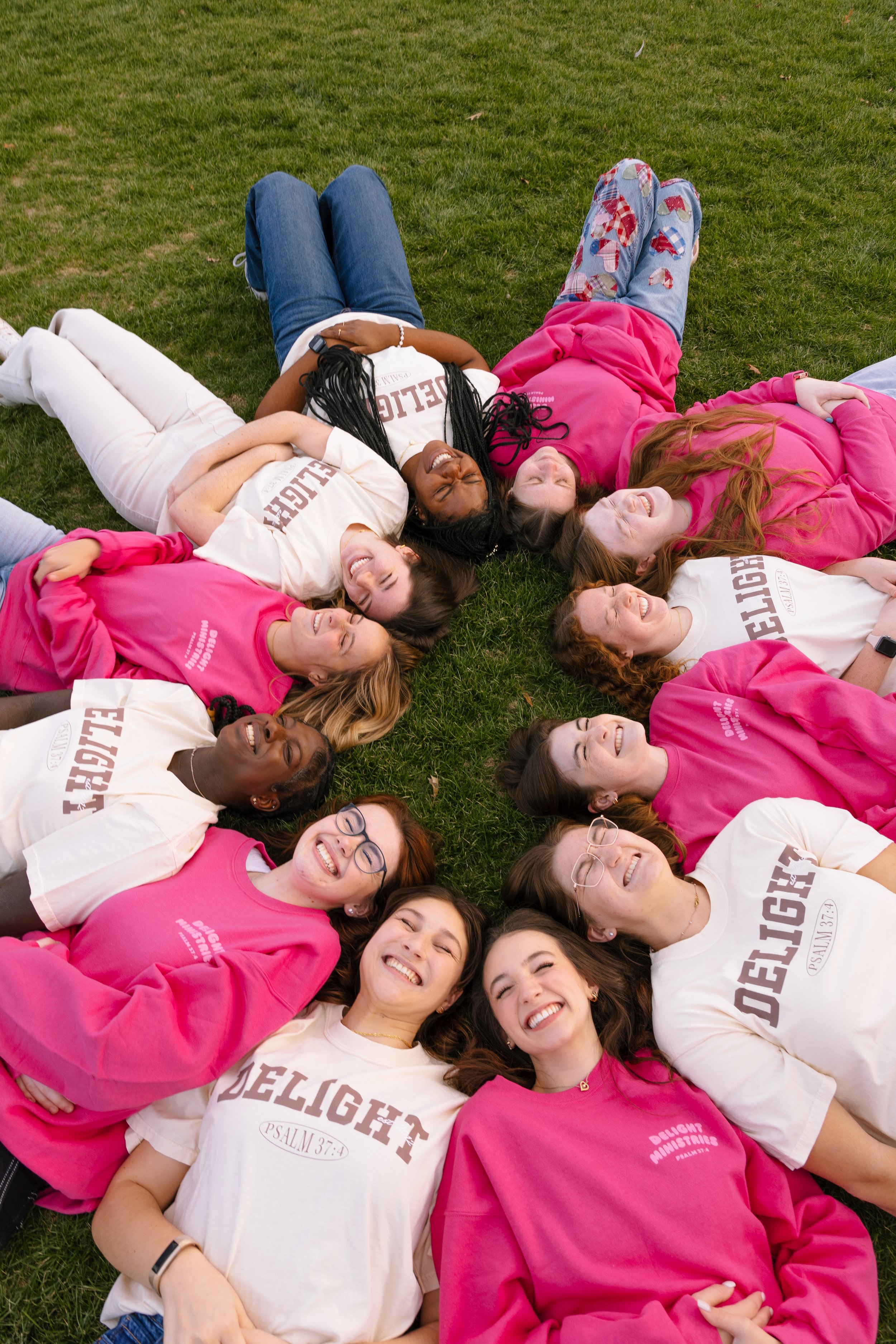 A picture of girls in Delight merch laying in a field in a circle smiling.