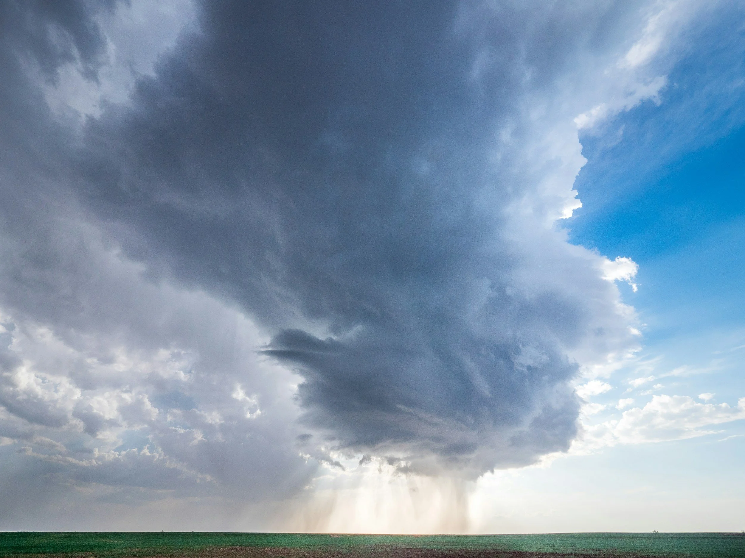 A dark supercell thunderstorm drops a heavy rain shaft over farmland, the type of severe weather behind Wisconsin's EF3 tornado and the emergency response housing Lima Charlie Inc. provides after disasters like it.