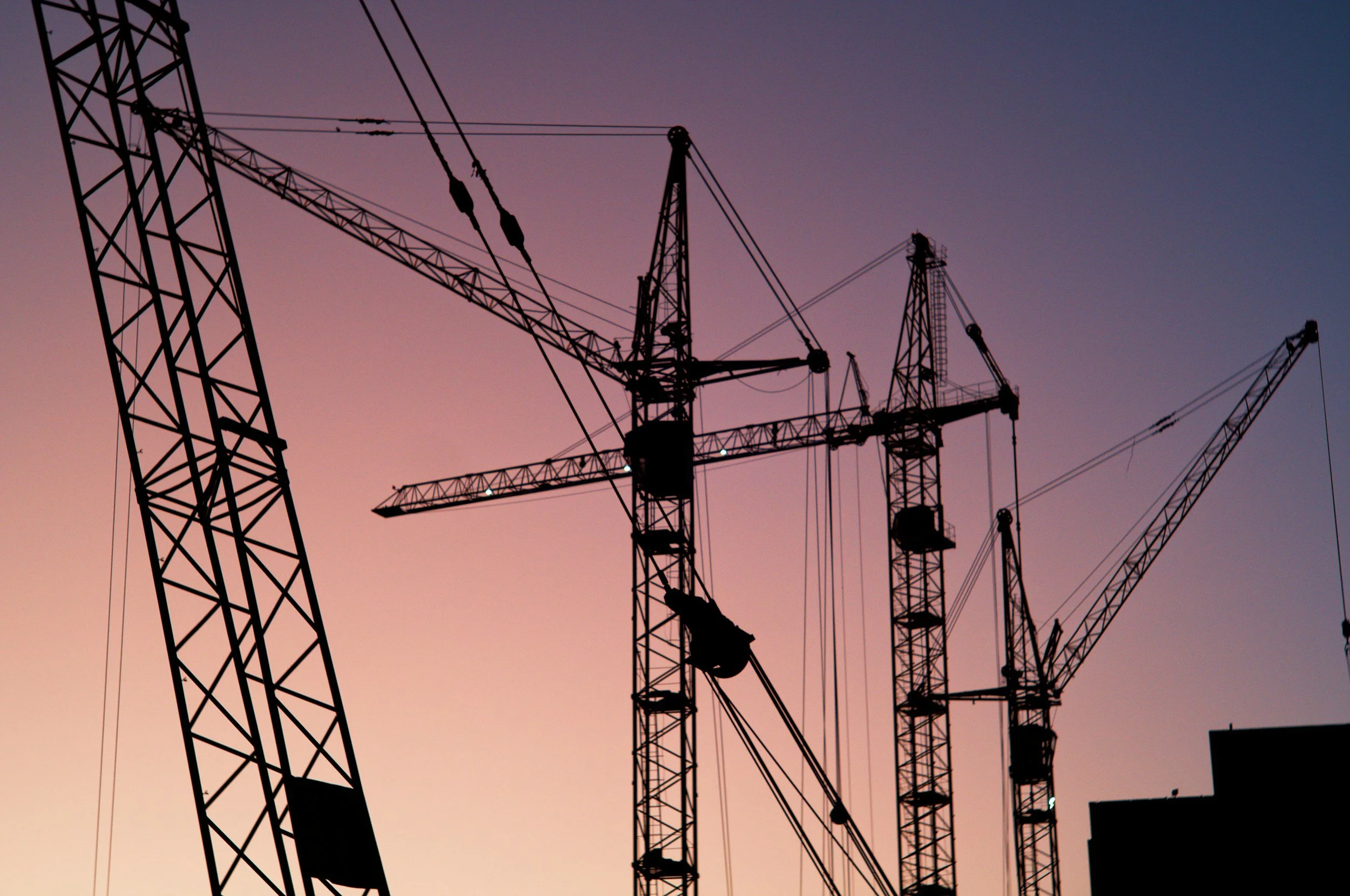 Tower cranes rise against a dusk sky at a construction site, the kind of large-scale fab build that creates the extended-stay corporate lodging demand Lima Charlie Inc. serves.
