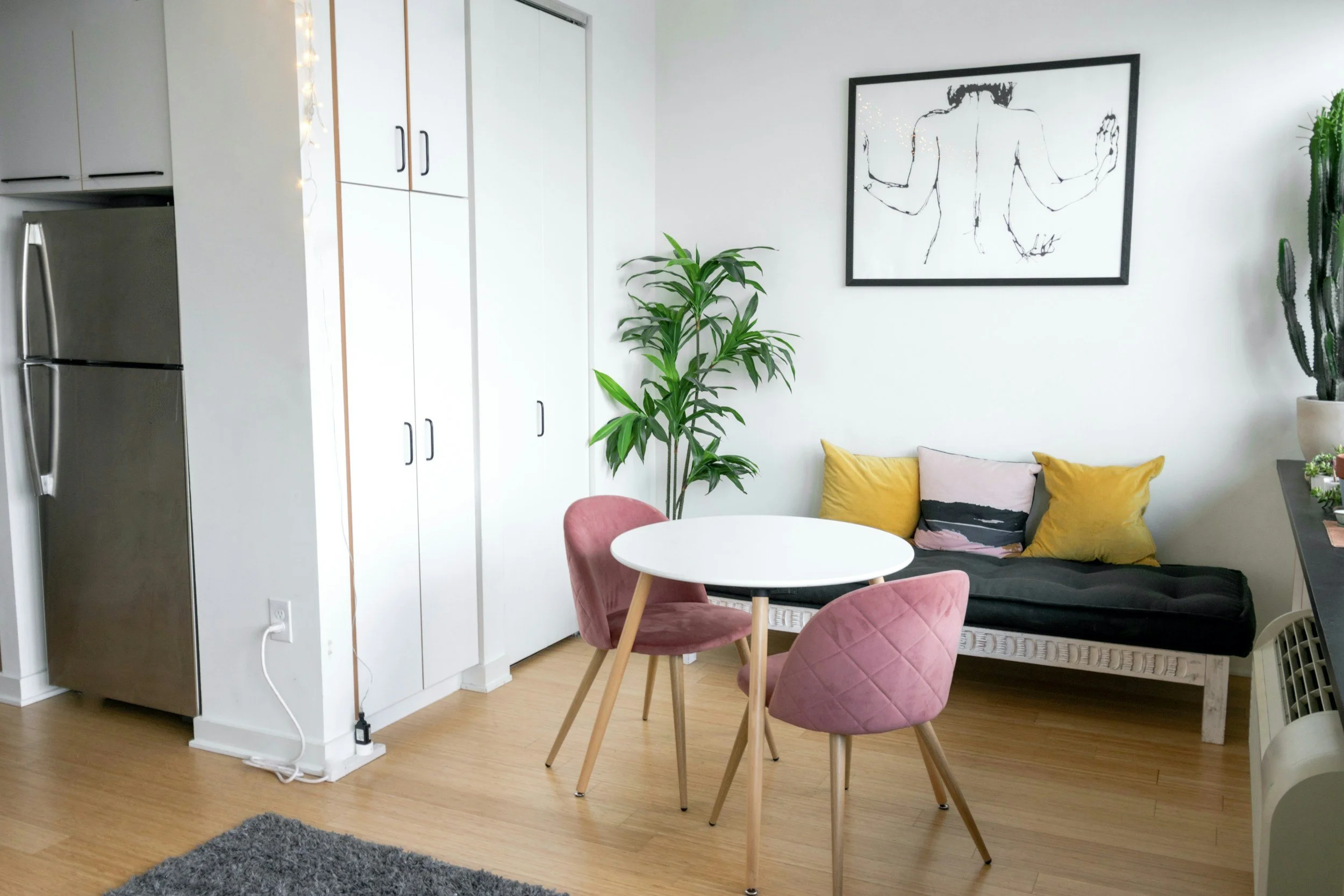 A furnished studio apartment features a small dining table, patterned throw pillows, and a leafy plant, the kind of corporate lodging Lima Charlie Inc. provides for relocated construction crews.