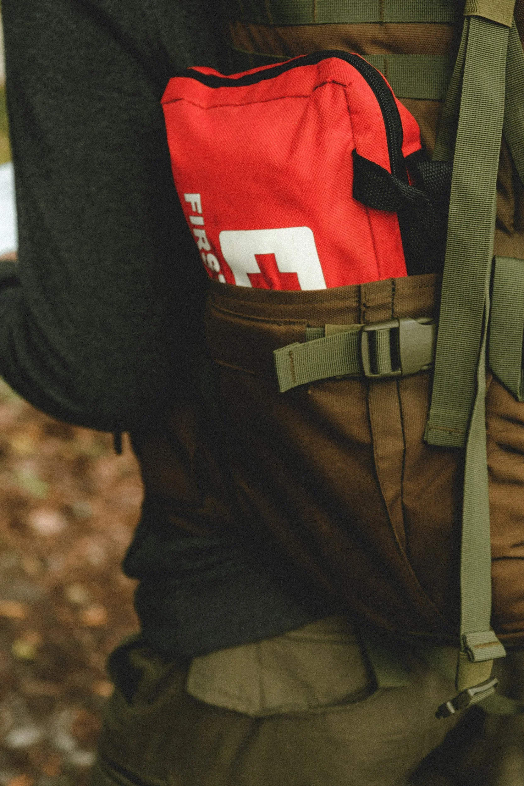 A red first aid kit sits strapped to a backpack, part of the emergency preparedness supplies Lima Charlie Inc. encourages every household to have ready before storm season peaks.