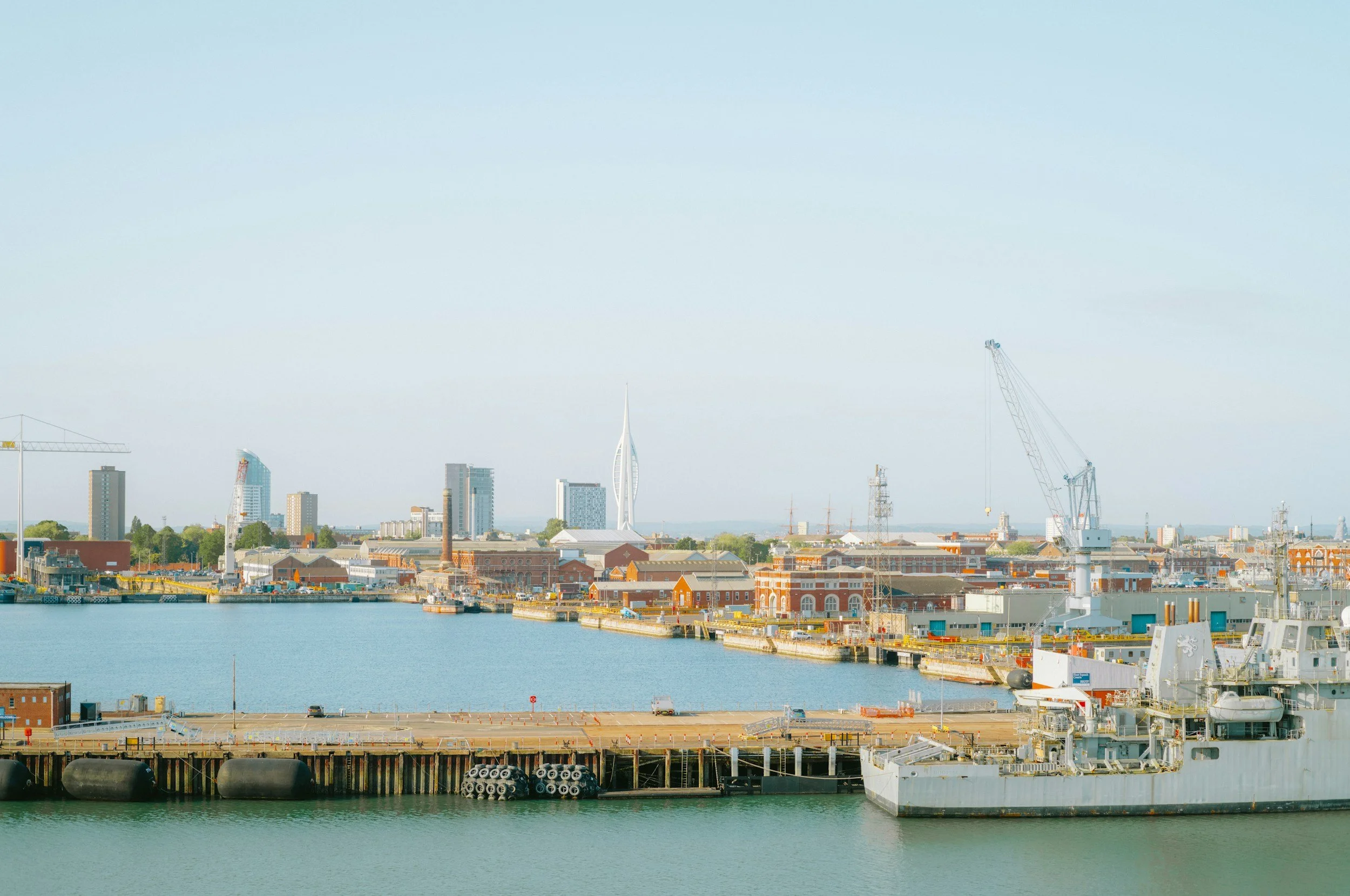 A naval shipyard waterfront shows ships docked alongside cranes and a city skyline, reflecting the kind of homeport region Lima Charlie Inc. serves with off-base military housing.