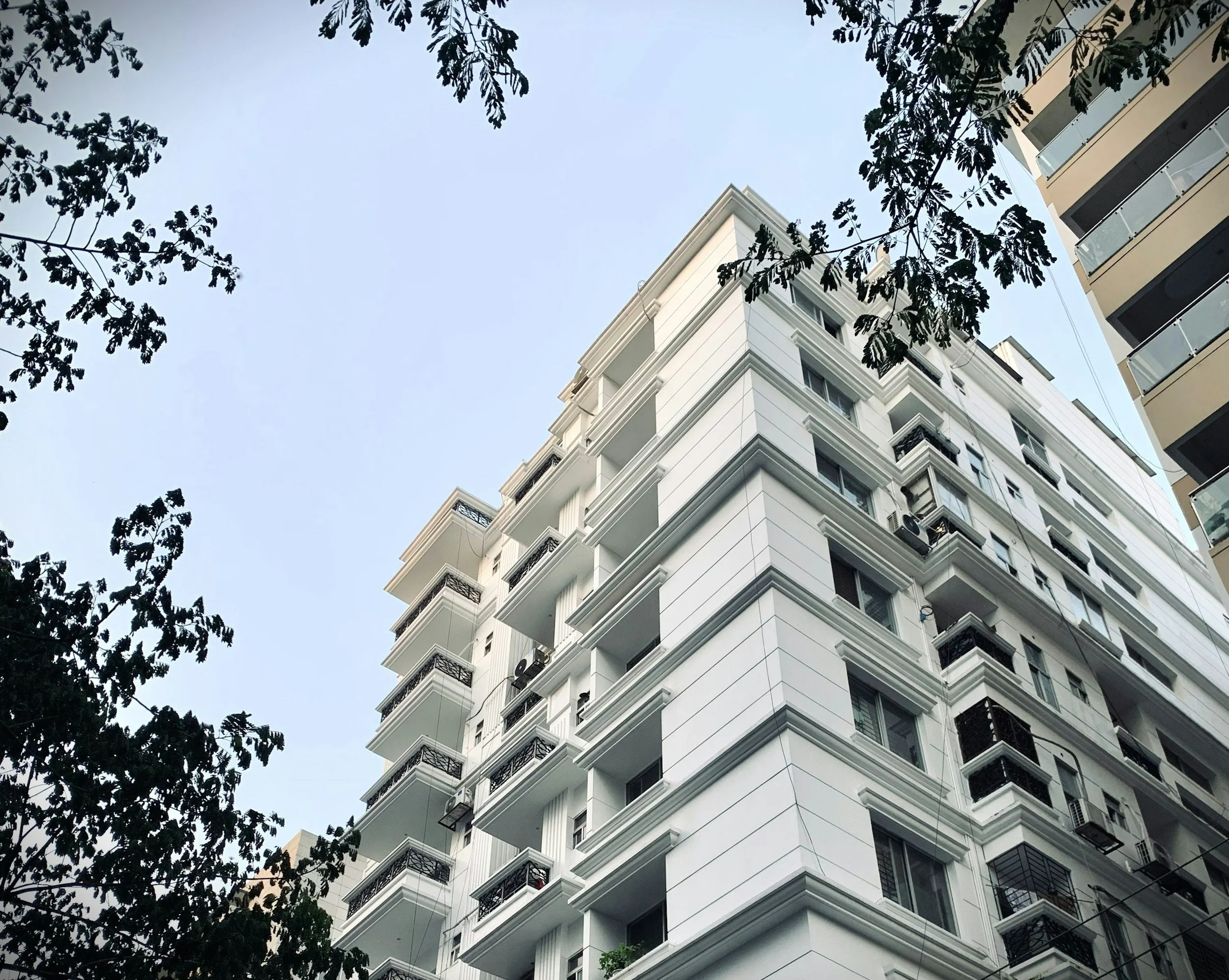 A tall white apartment building rises above tree branches, representing the kind of new-city housing market employees navigate with Lima Charlie Inc.'s corporate relocation support.