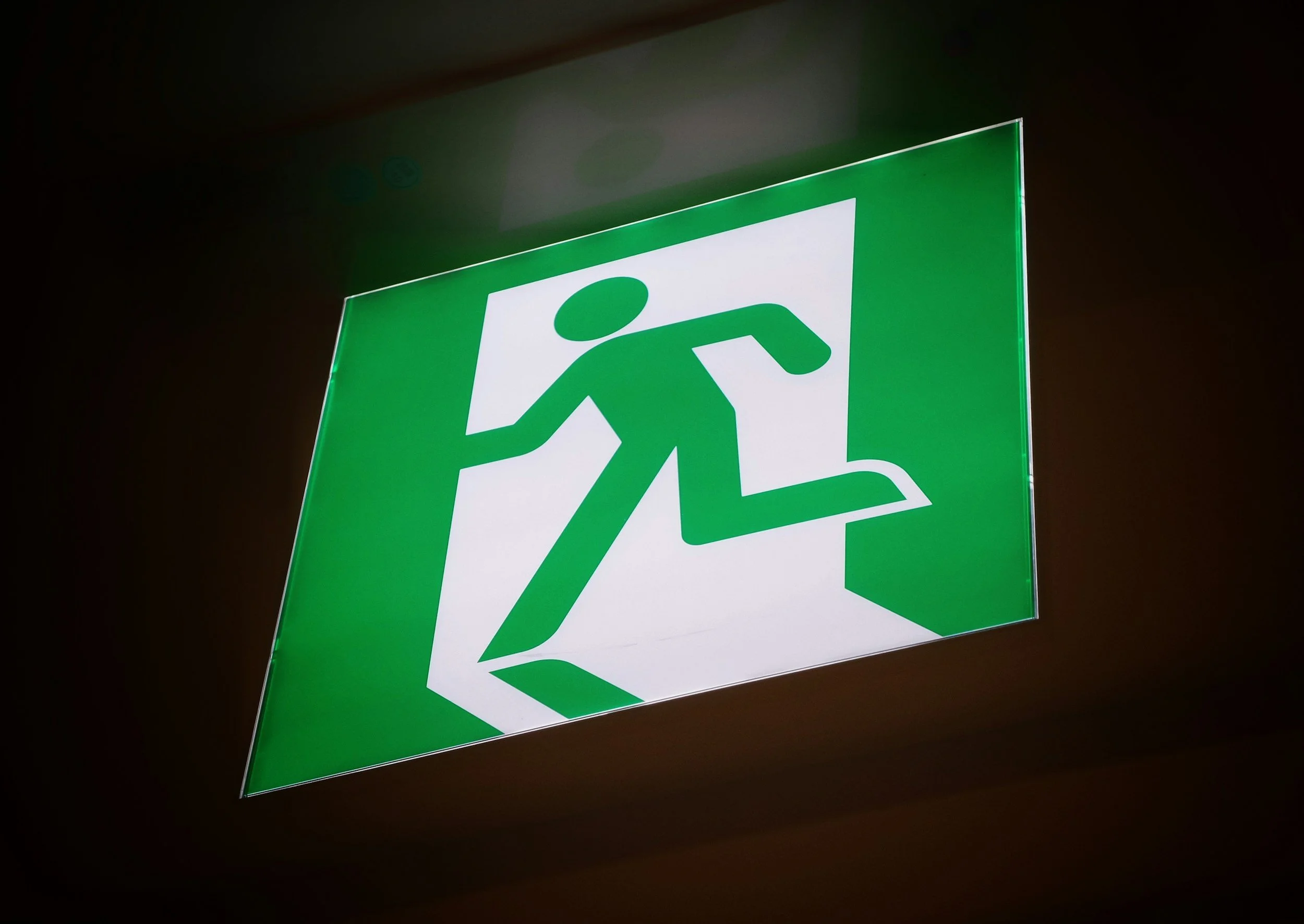 An illuminated green emergency exit sign points the way out, reflecting the evacuation planning Lima Charlie Inc. encourages families to have in place before a storm forms.