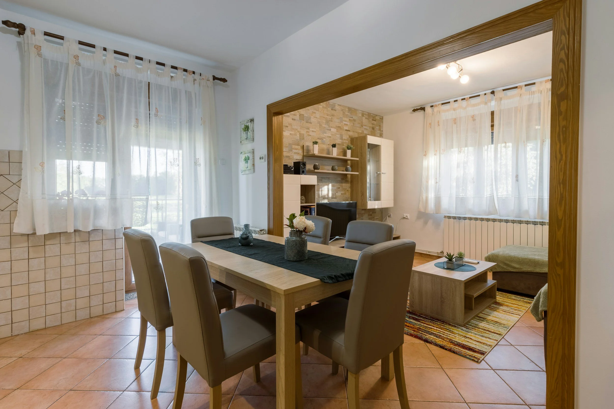 A bright dining and living area with a wooden table and sheer curtains shows the kind of comfortable, furnished home Lima Charlie Inc. provides service members and their families.