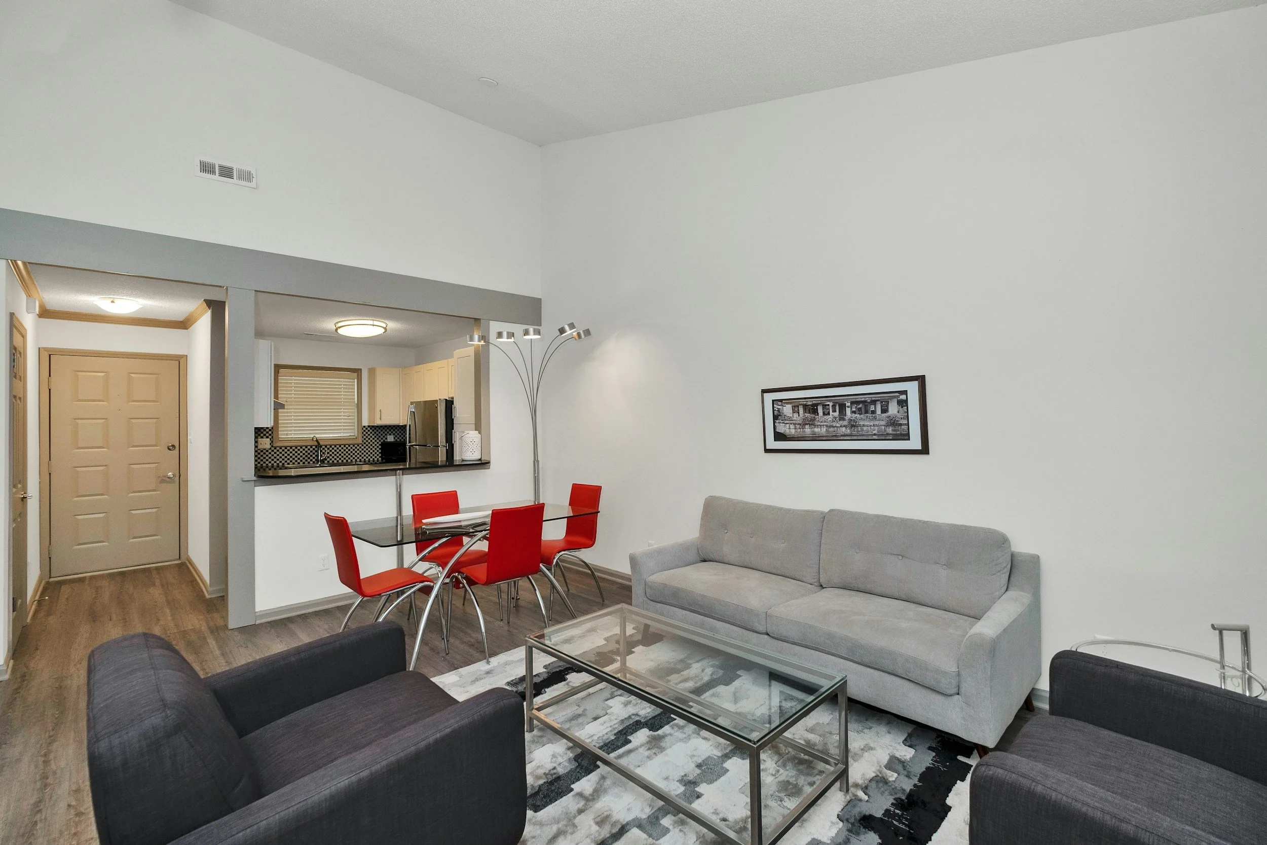 A modern furnished living room with gray sofas and red dining chairs shows the kind of rental housing Lima Charlie Inc. provides service members who choose to rent while evaluating their local market.