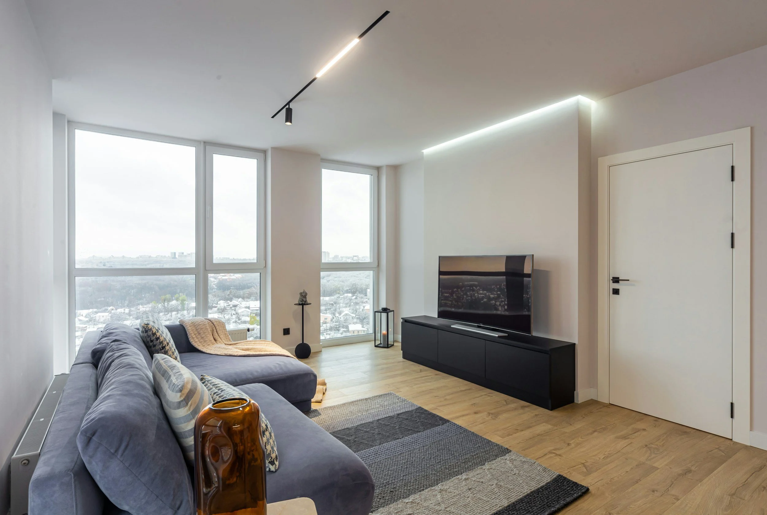 A modern high-rise living room with floor-to-ceiling windows and a city view shows the kind of furnished corporate apartment Lima Charlie Inc. provides employees relocating into growing Sun Belt markets.