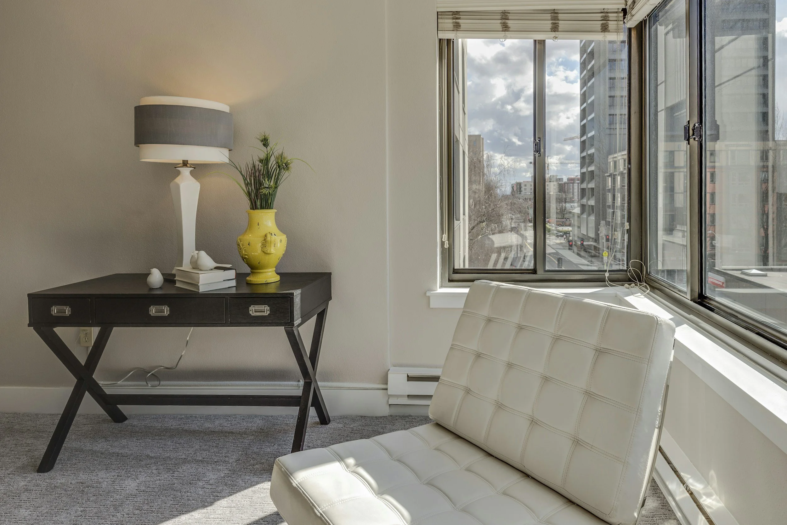 A furnished living space with a desk, lamp, and chair beside a city window, the kind of move-in ready housing Lima Charlie Inc. provides as an emergency housing partner."