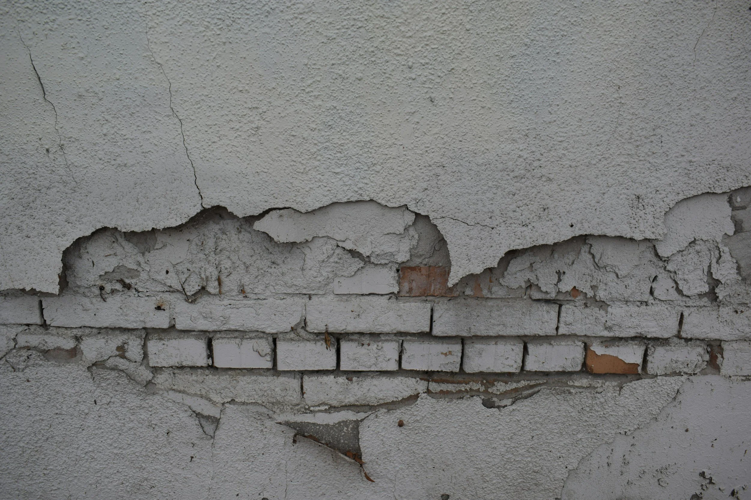 A cracked and crumbling exterior wall with exposed brick, the structural damage that leads families to Lima Charlie Inc. for earthquake displacement housing