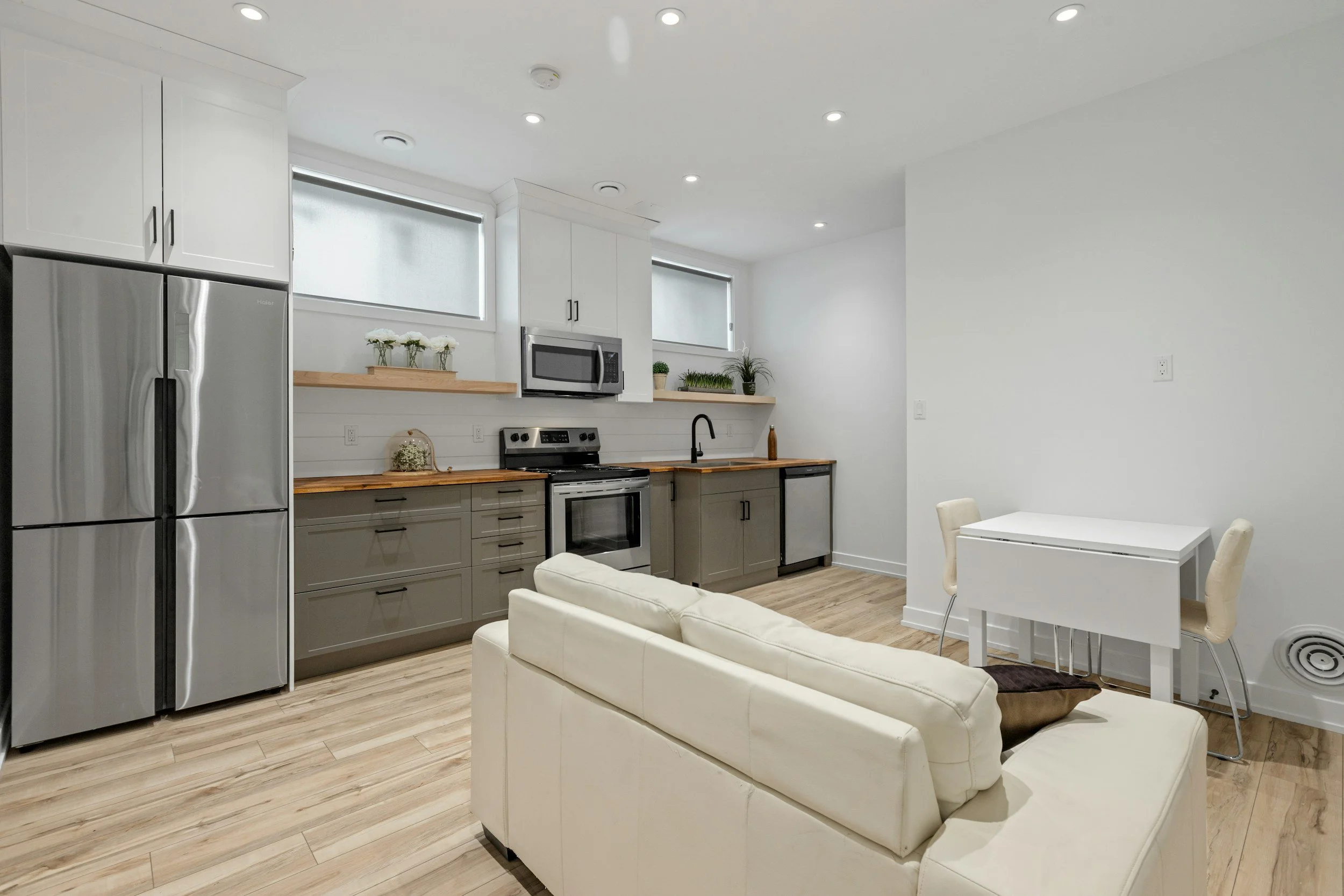 A fully furnished open-concept kitchen and living room with stainless steel appliances and a white sofa, the move-in ready housing Lima Charlie Inc. provides.