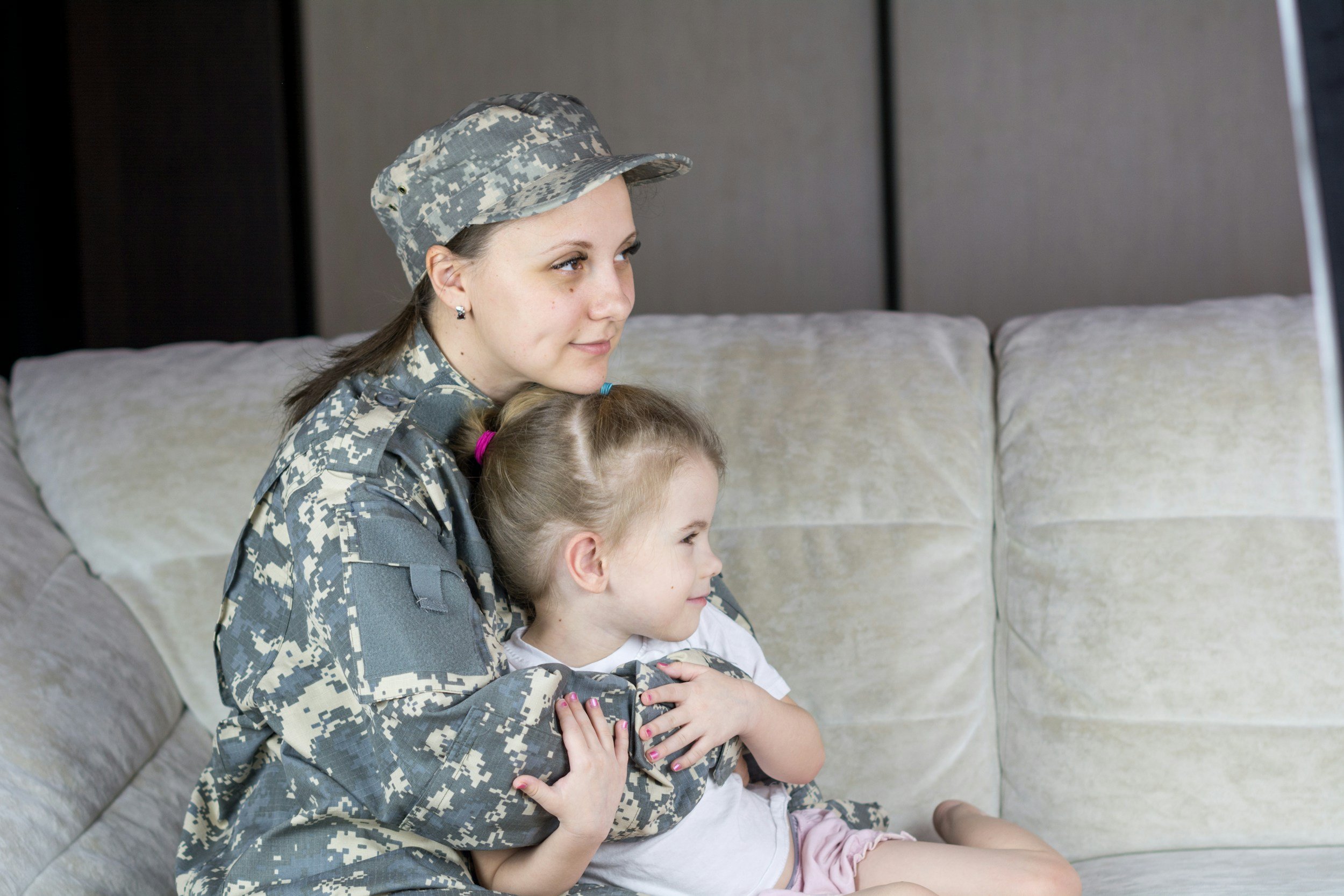A service member in uniform holding her young daughter on a couch, the military families Lima Charlie Inc. supports through PCS moves to and from Guam.