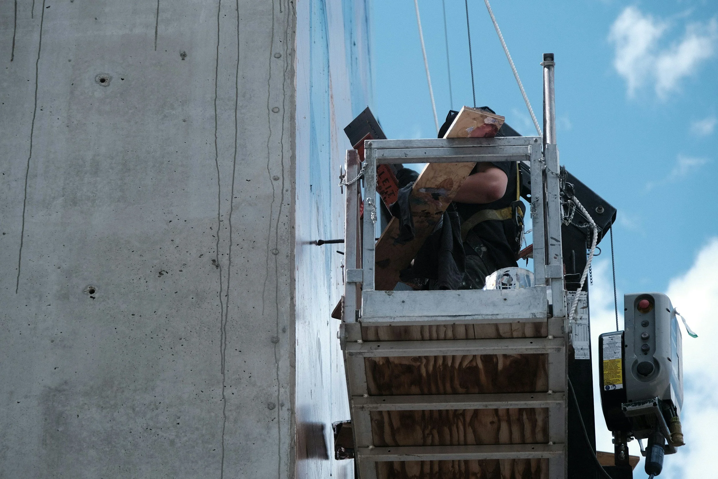 A worker in a lift basket beside a concrete wall under a blue sky, the kind of crew work Lima Charlie Inc. supports with corporate lodging during storm recovery.