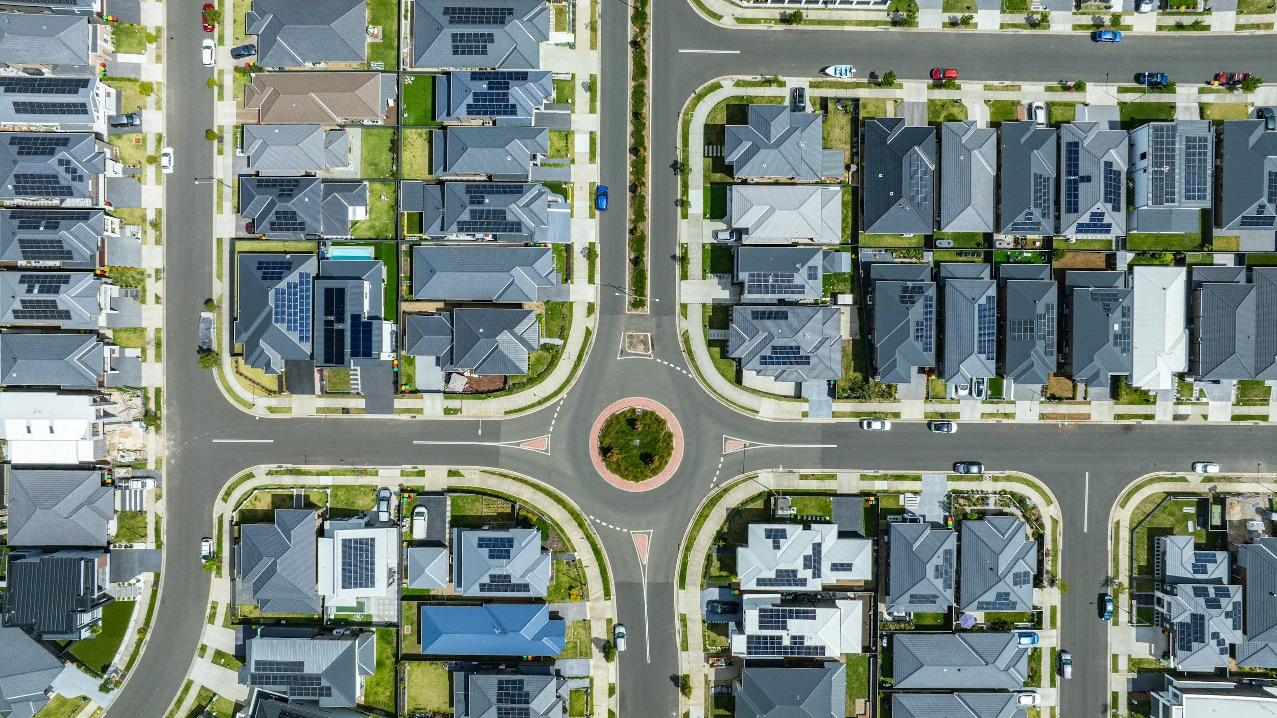 Aerial view of a suburban neighborhood with rooftop solar panels around a roundabout, the county-level housing Lima Charlie Inc. helps states map for state disaster housing.