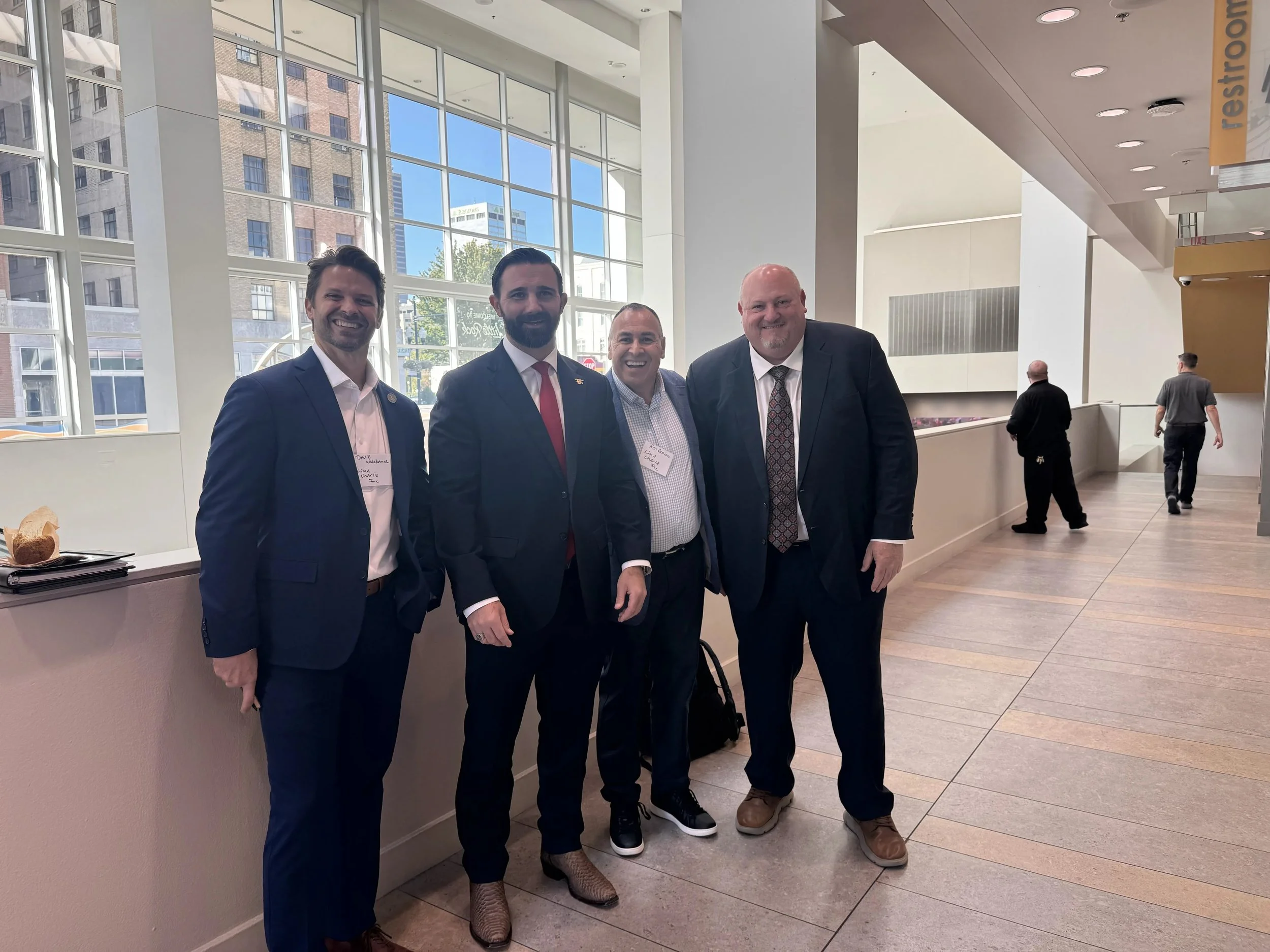 David Waldbauer and Ron Cedillo of Lima Charlie Inc. smiling with two other attendees in a convention center hallway at the NEMA Annual Forum in Little Rock.