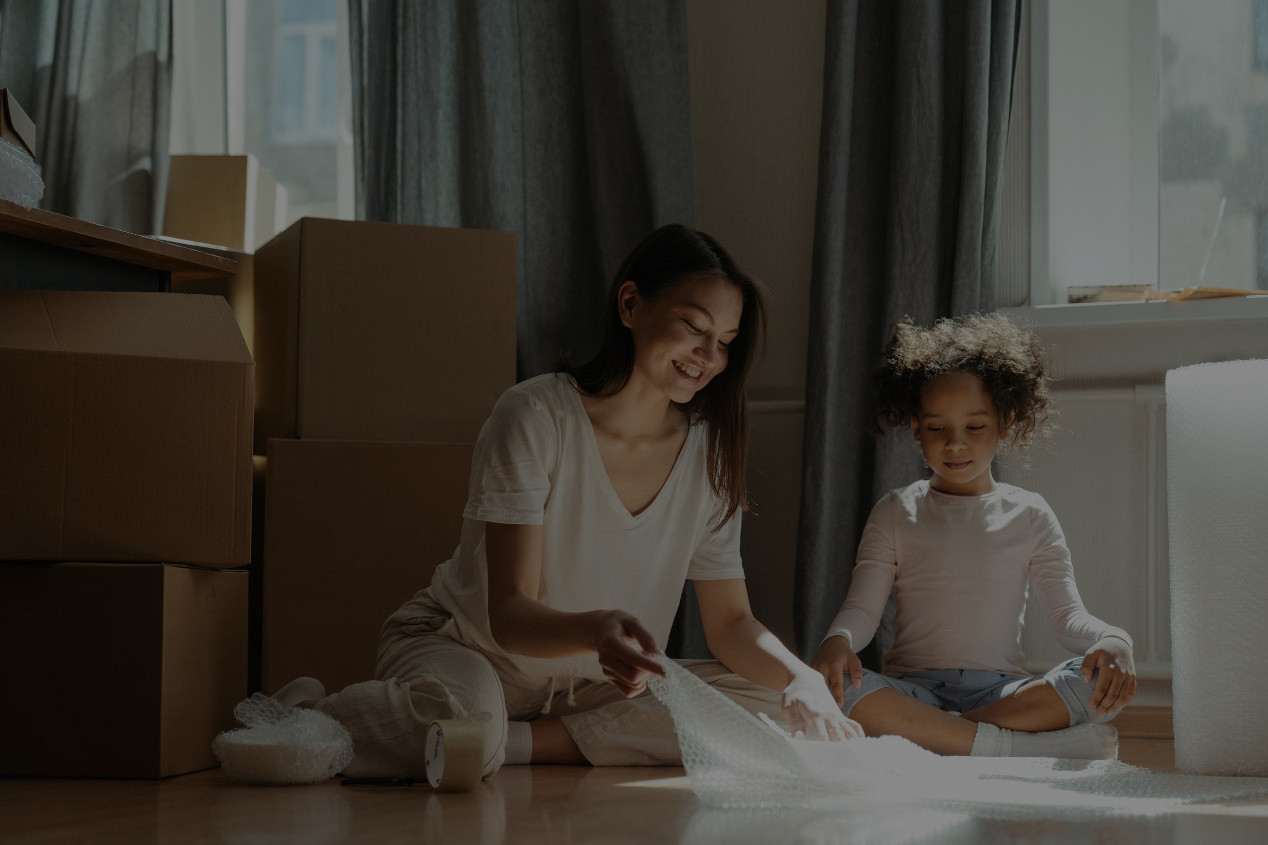 A woman and young girl surrounded by boxes. Lima Charlie Inc. provides housing solutions for families during disaster recovery, ensuring comfort and security.
