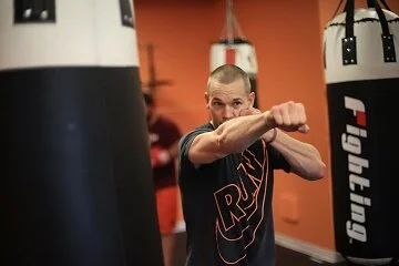 A man practicing boxing punches at a gym with punching bags.