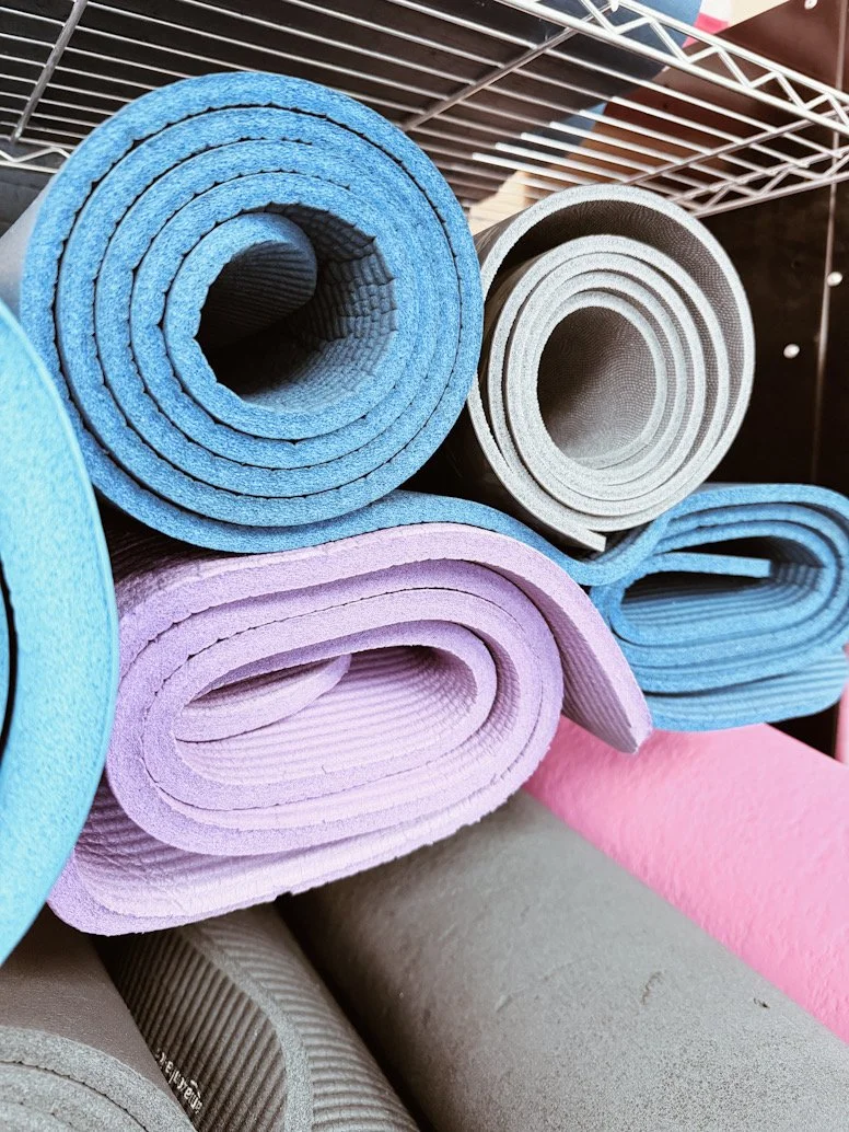 Multiple rolls of colorful yoga mats, including blue, pink, purple, gray, and beige, stored on a wire shelf.