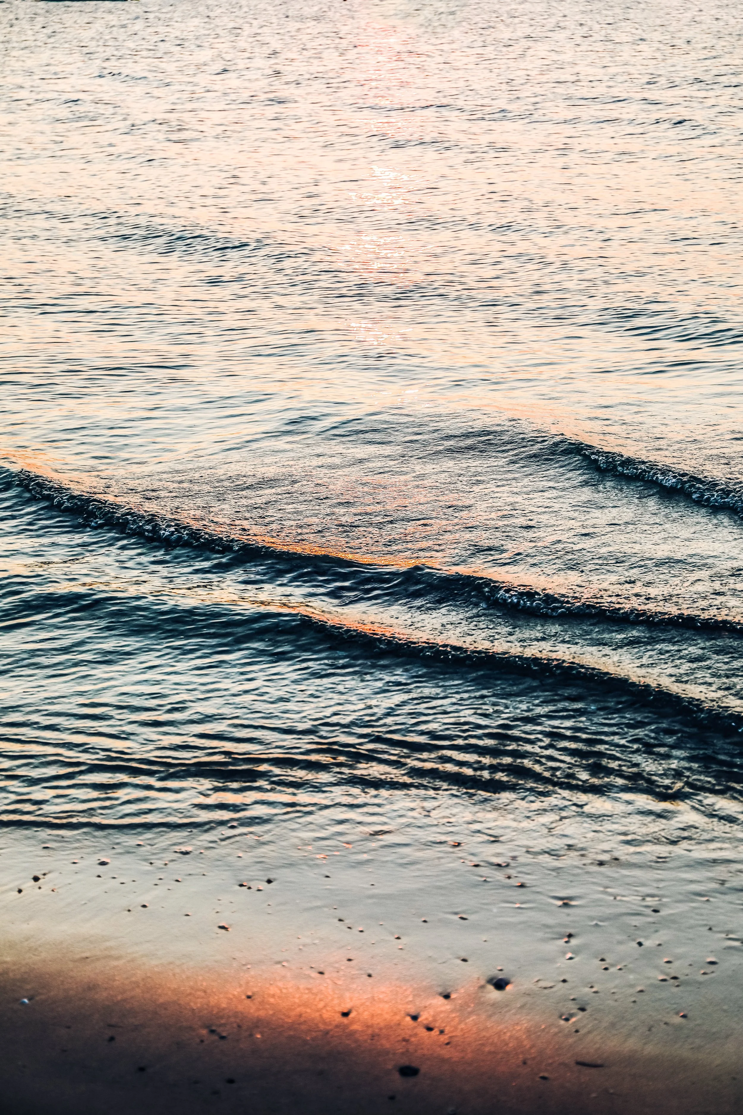 Sunset over the water with gentle waves on the beach.