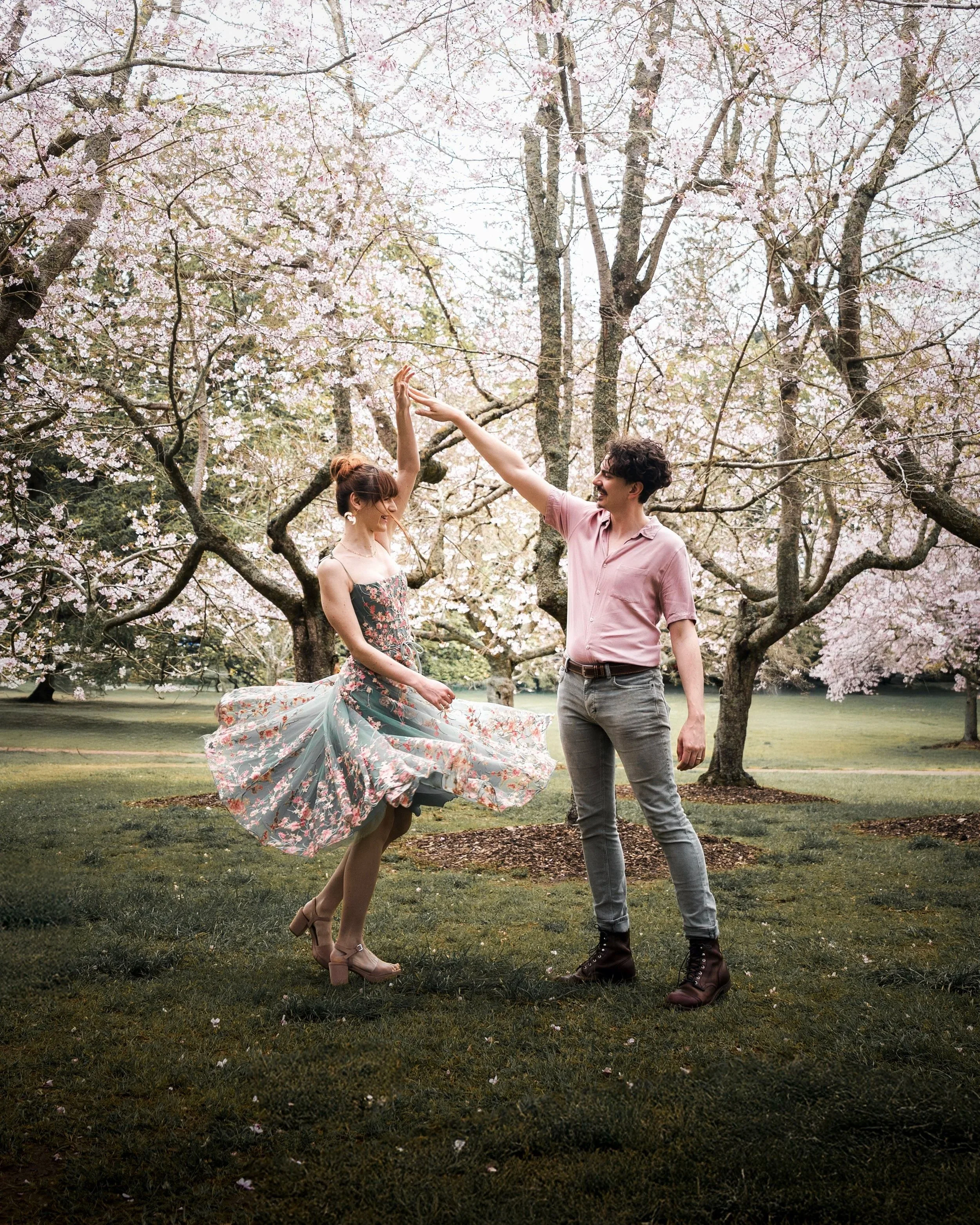 A couple dancing outdoors under blooming cherry blossom trees in a park during spring.