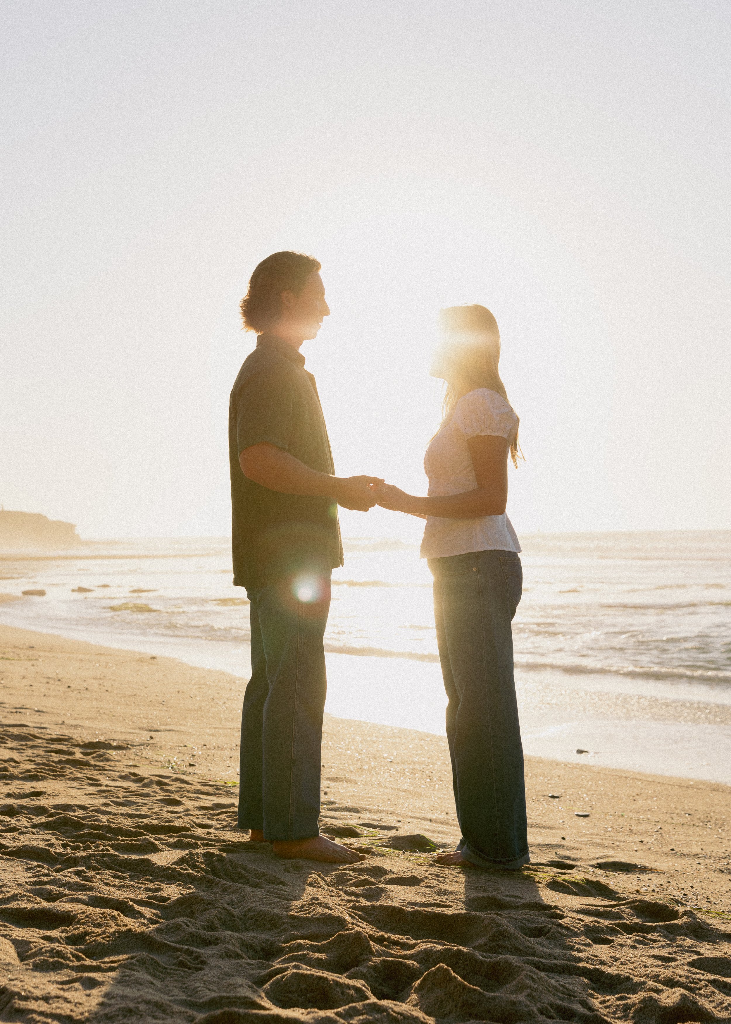 A couple holding hands on a beach at sunset.