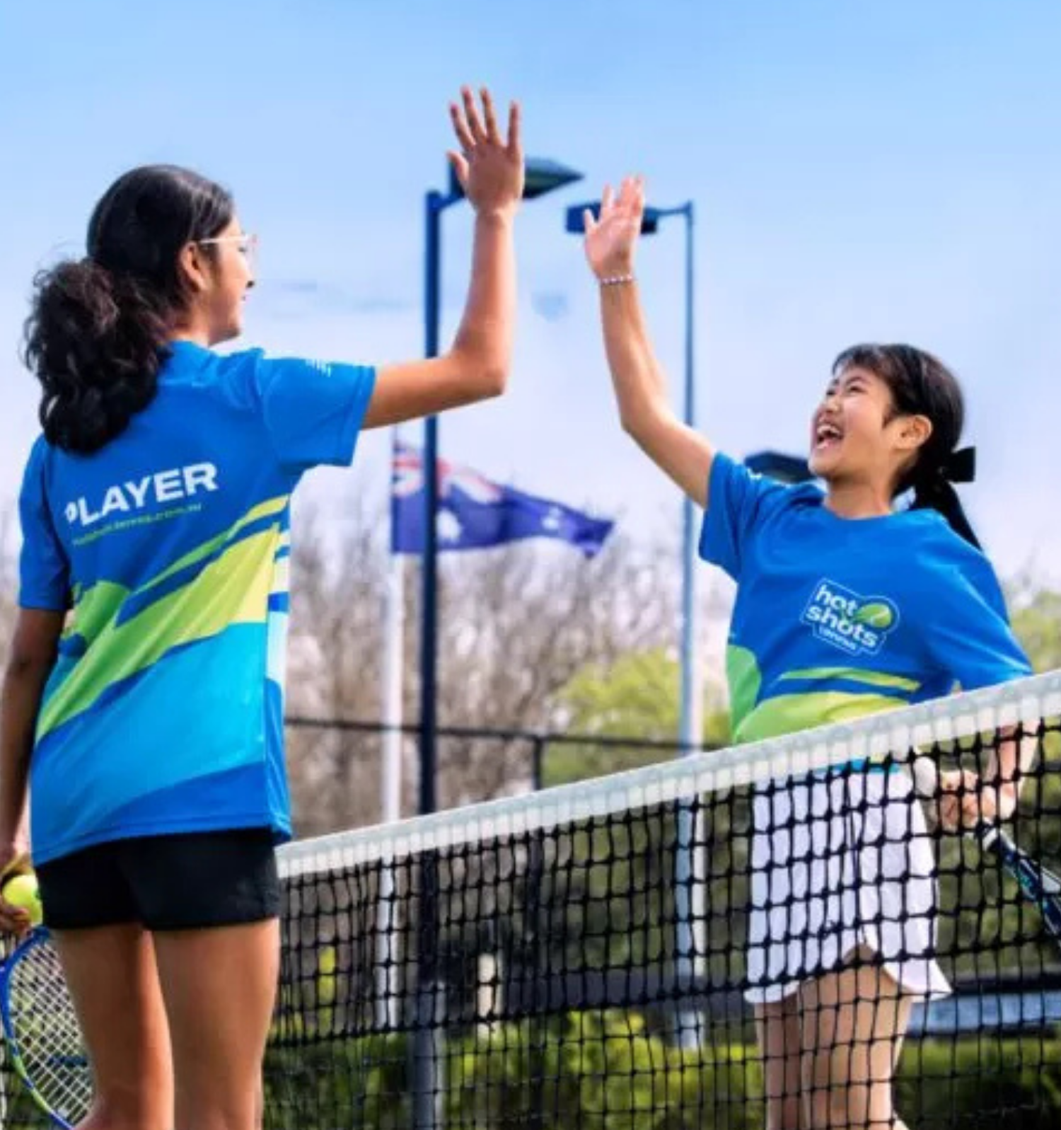 Two junior tennis players high-five over the net during a semi-private coaching session.