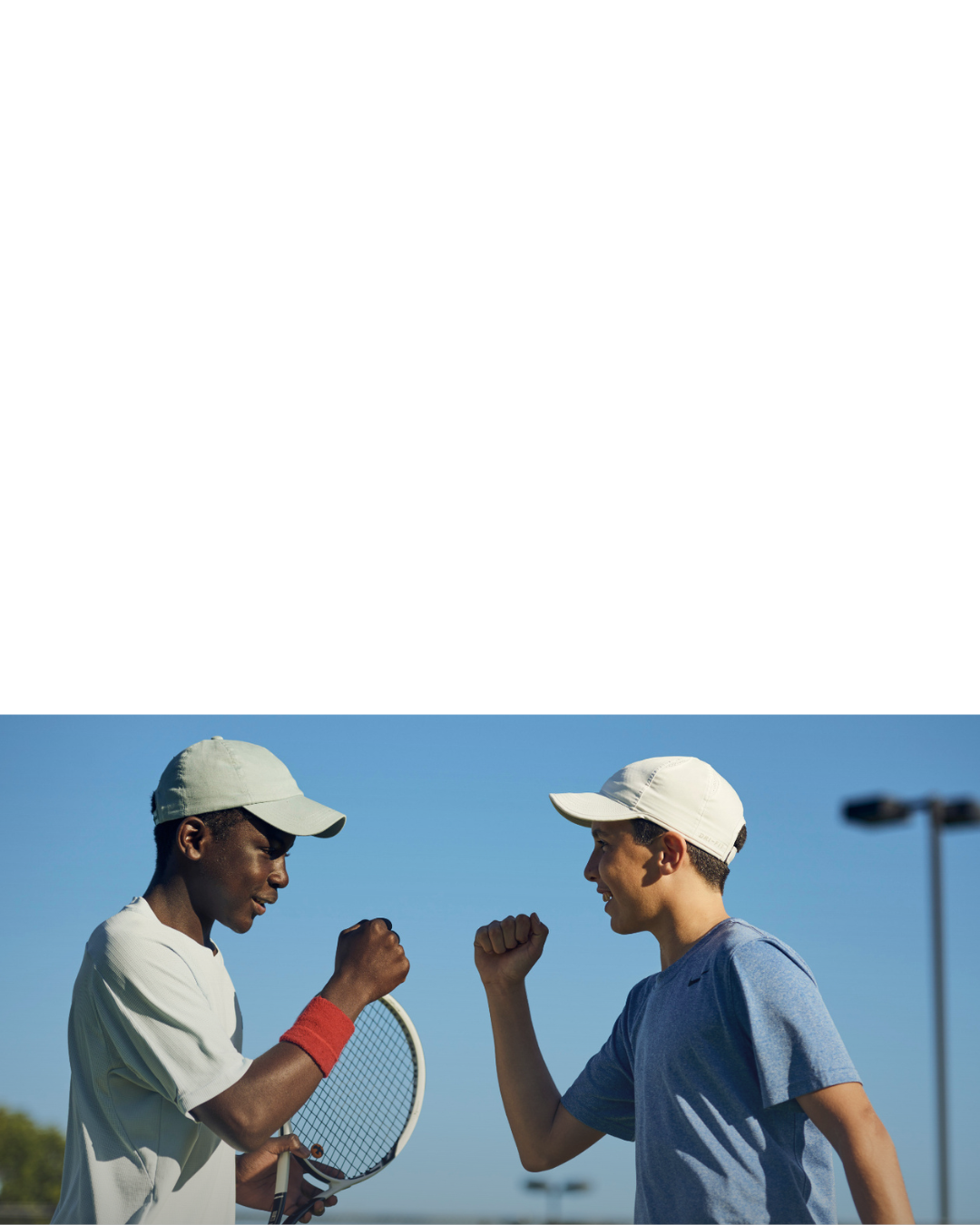Two young tennis players fist-bumping on a court, holding racquets and smiling during a practice session.