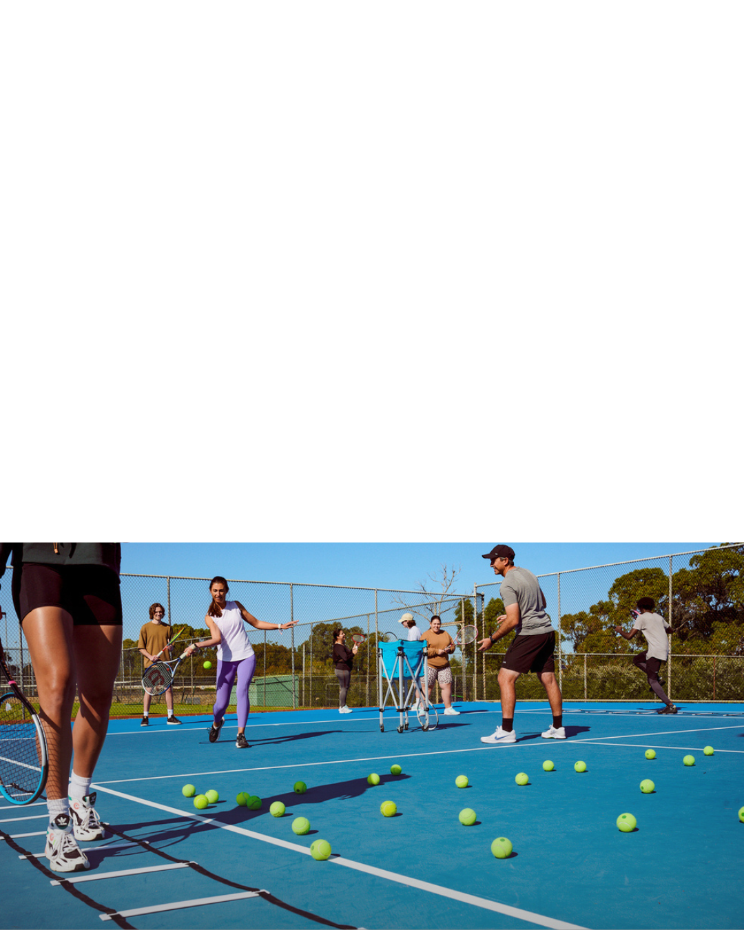 Adult players taking part in a group tennis coaching class with drills and ball exercises on an outdoor court.