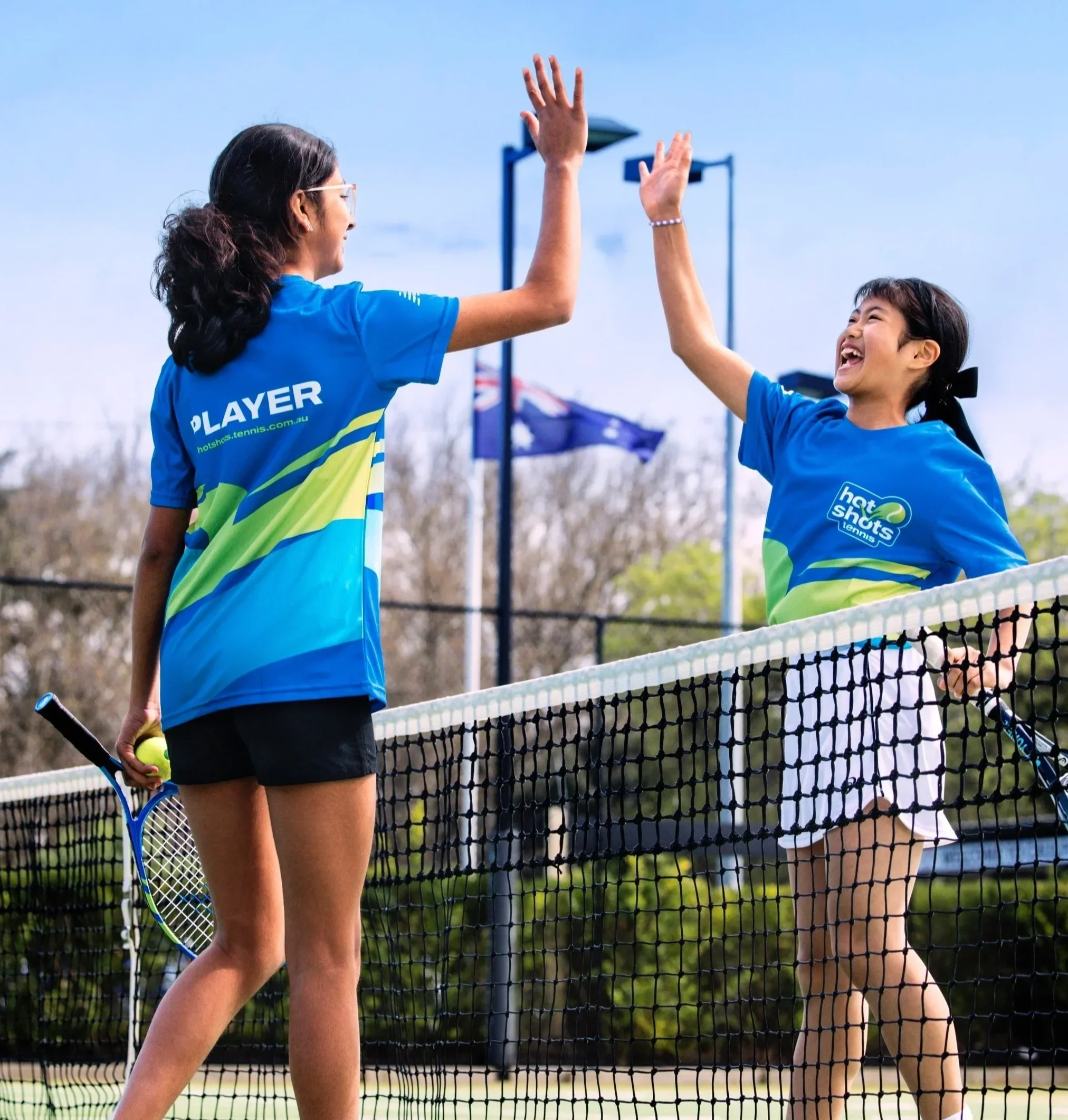 Two junior tennis players high-five over the net during a semi-private coaching session.