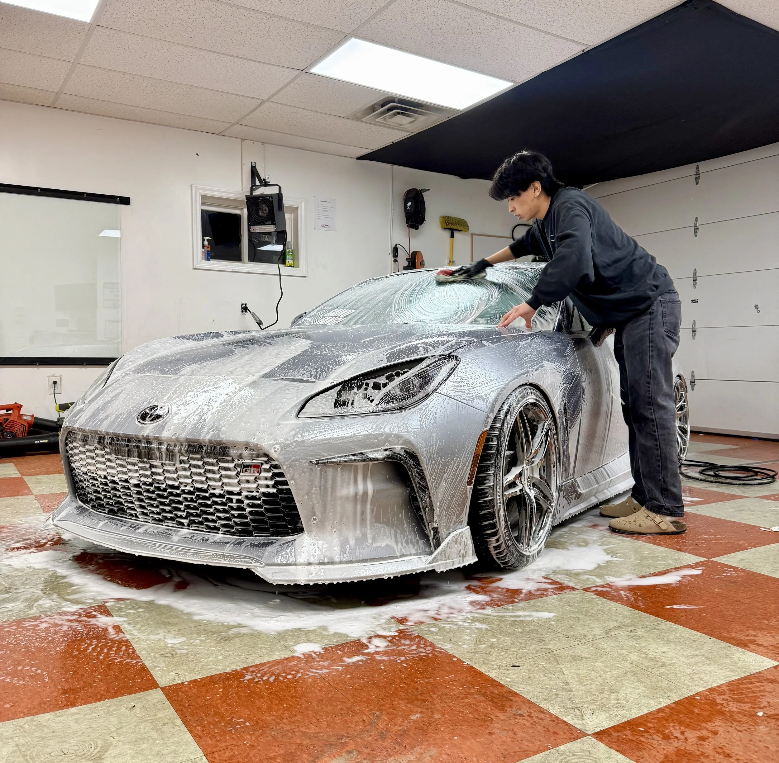 A sleek coupe covered in thick snow foam during a professional decontamination wash for ceramic coating prep.