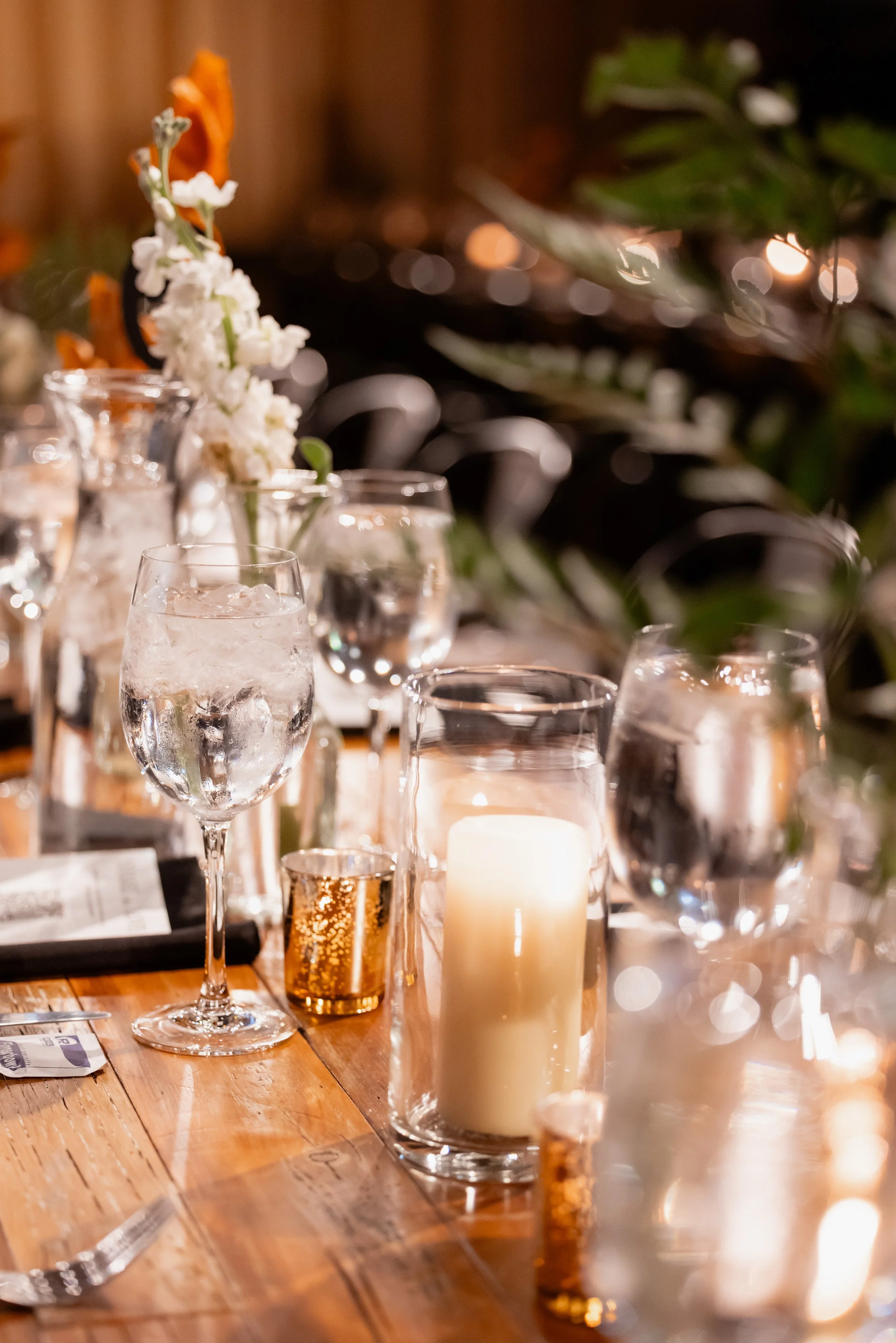 Close-up of a reception table with candlelight, glassware, and floral details.