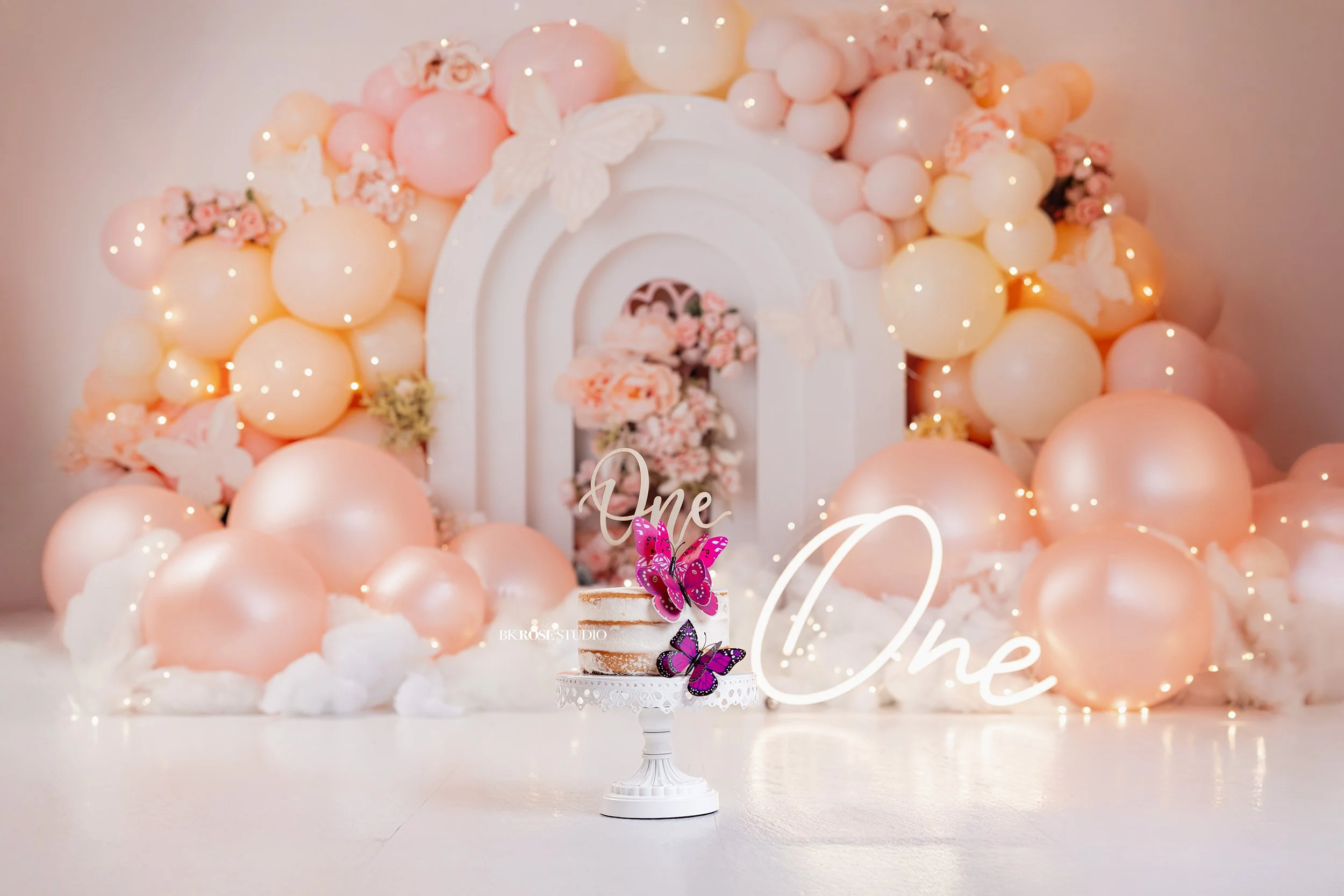 colorful cake smash backdrop with peach and yellow balloons with butterlies and a cake