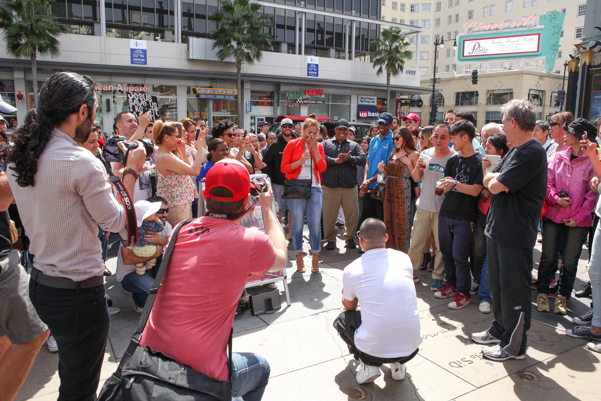 woman getting proposed to by her boyfriend with a large crowd of people gathered around on a busy city street