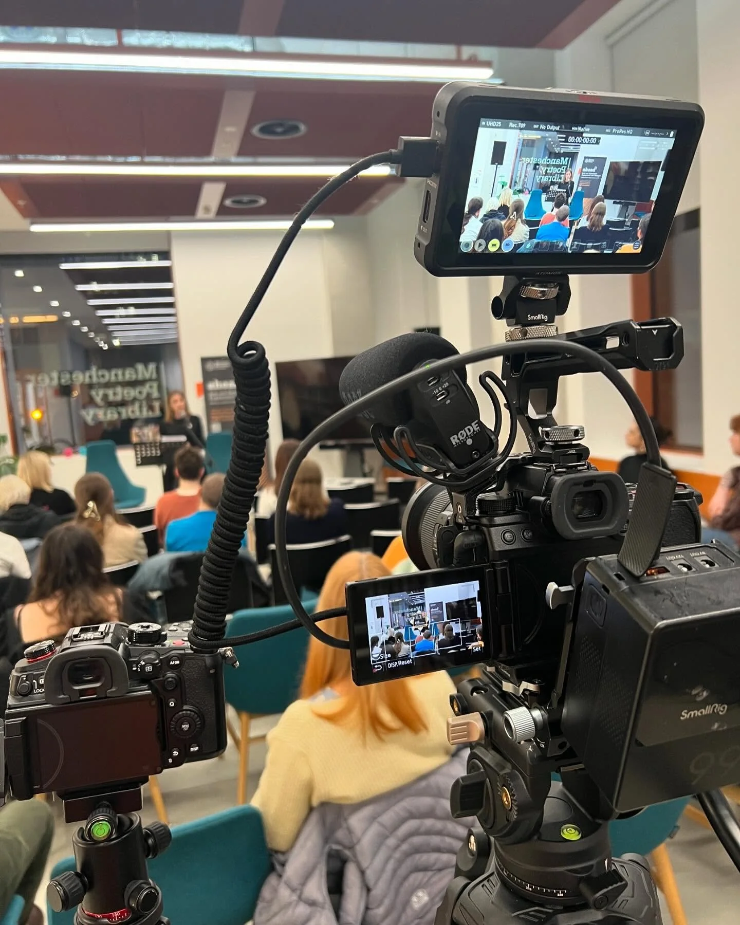 Camera setup recording a presentation at a conference in a room with audience members seated and listening.