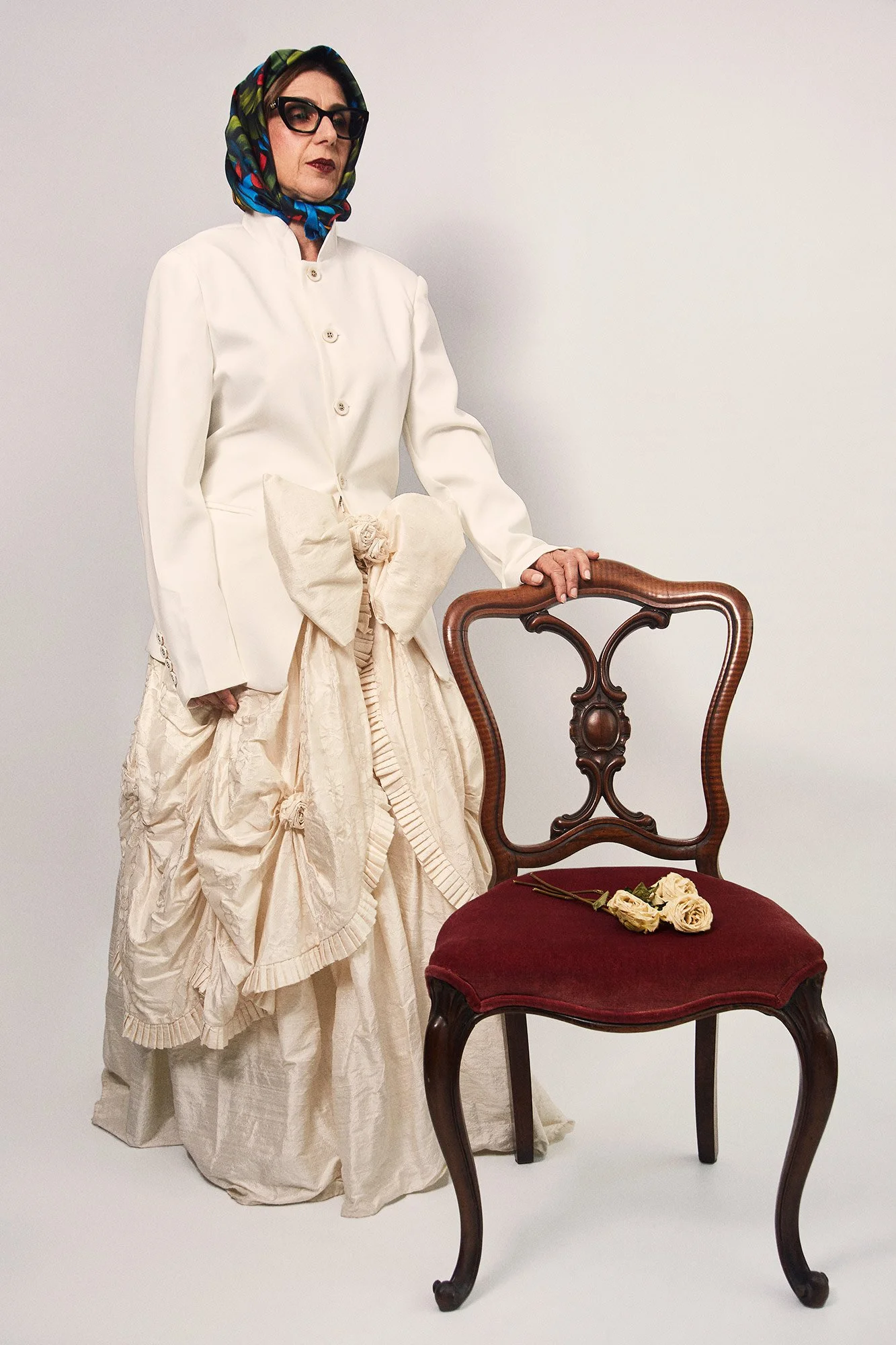 Portrait photograph of La Abuela standing beside a chair from the series Cuerpo Vestido, Alma Desnuda by Beatriz Perez.