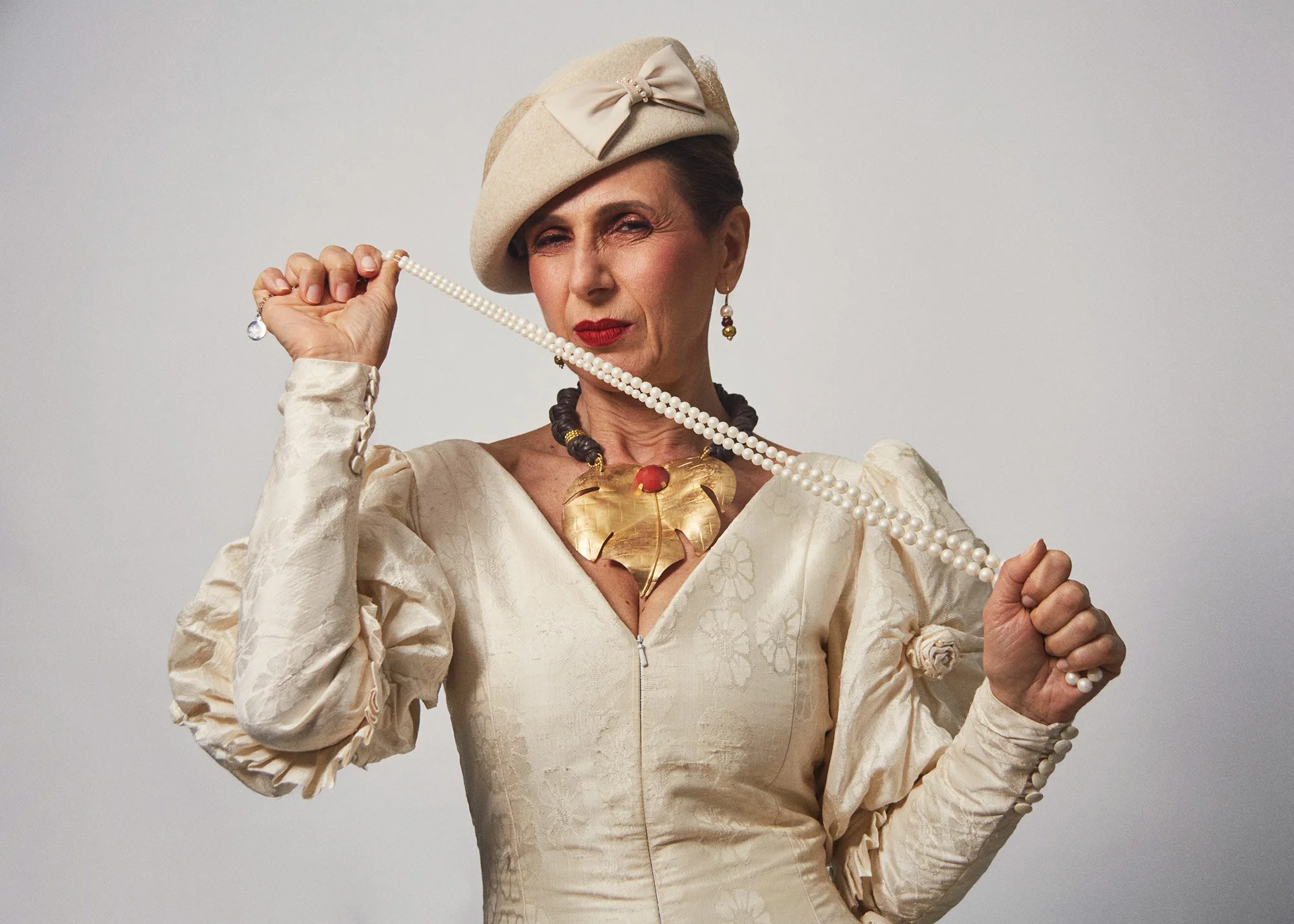 Portrait photograph of La Doña playing with a pearl necklace in a performative gesture from the series Cuerpo Vestido, Alma Desnuda by Beatriz Perez.