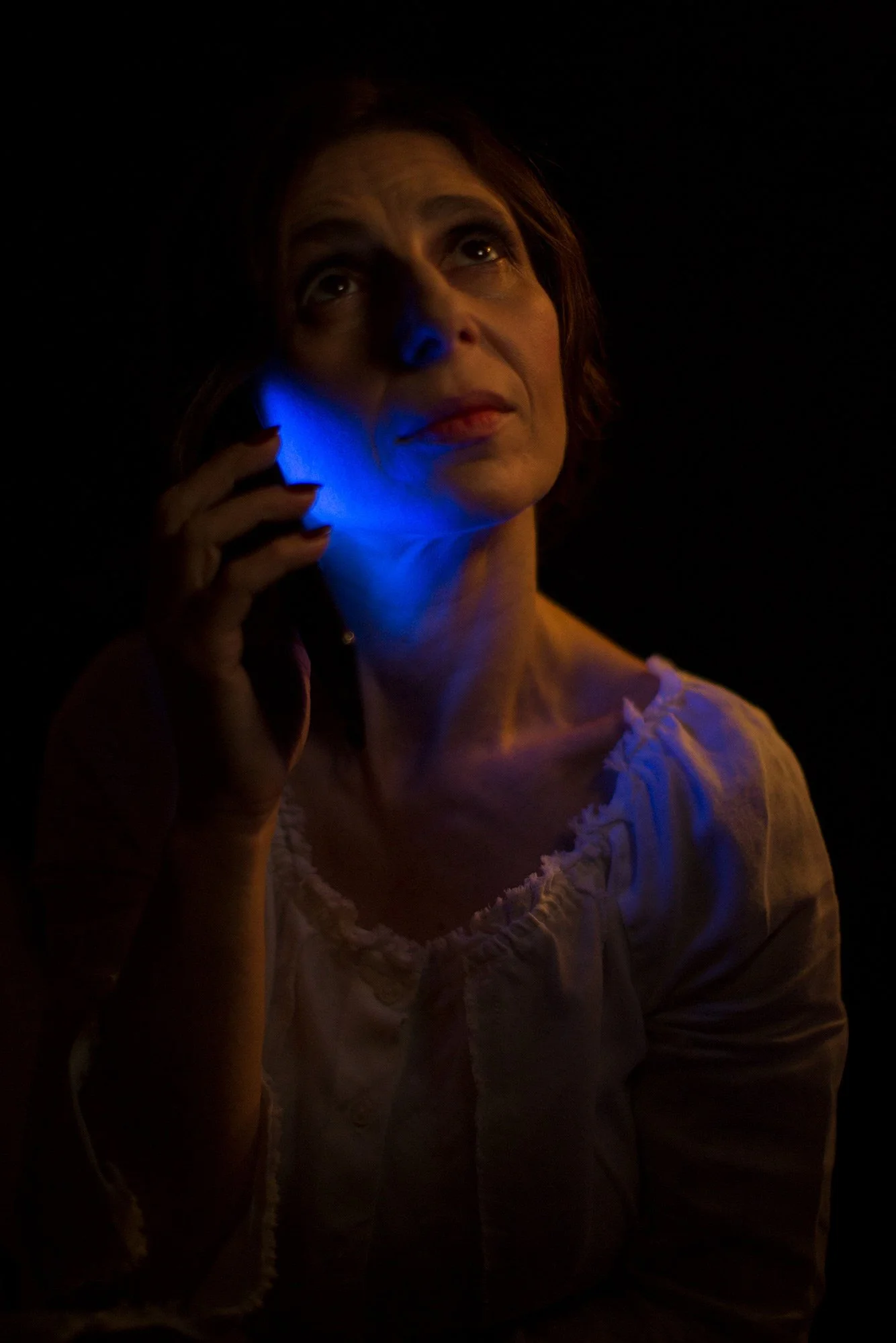 Dimly lit portrait of a woman speaking on a mobile phone from The Weeping Woman series by Beatriz Perez.
