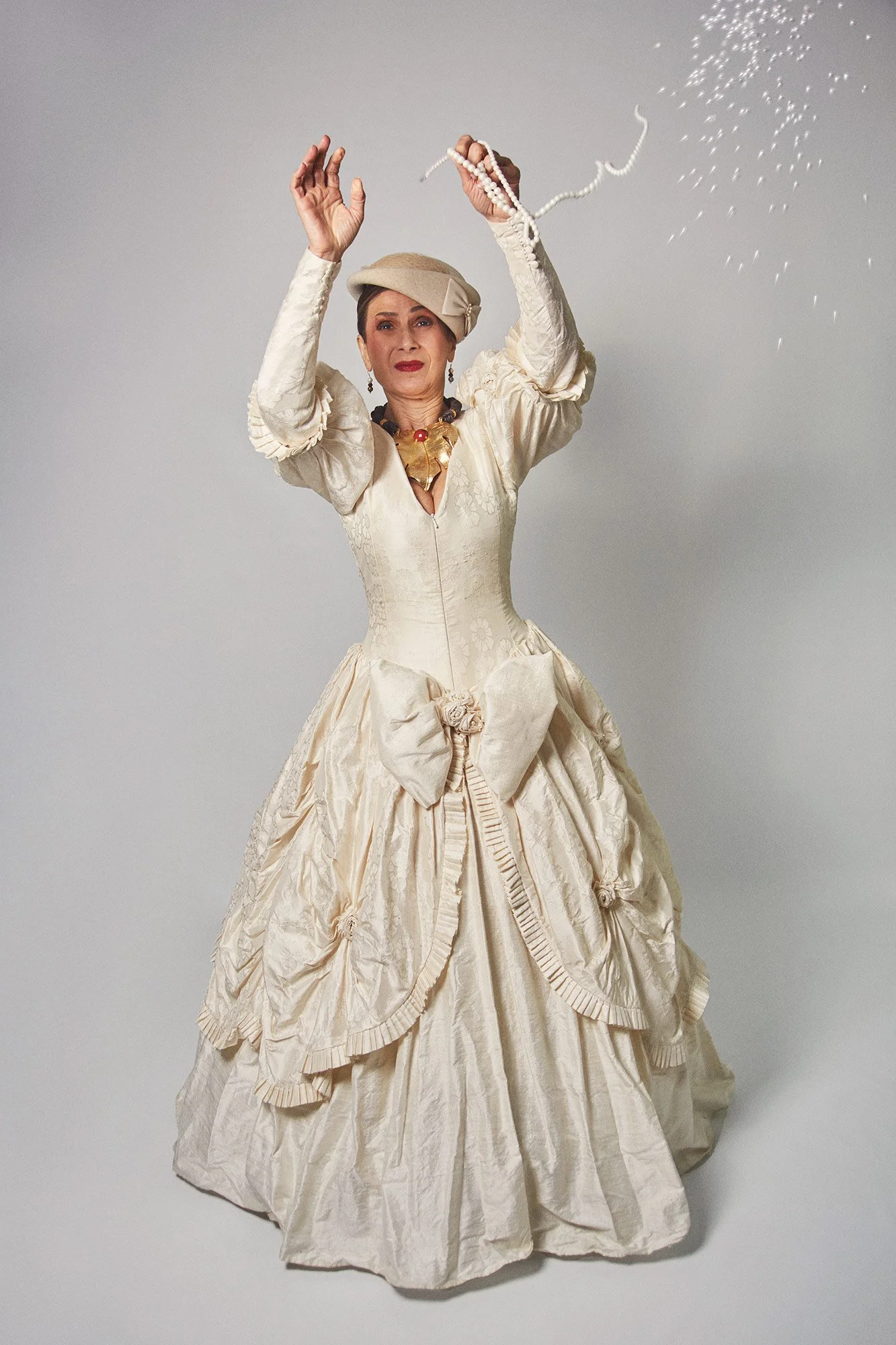 Photograph of La Doña breaking a pearl necklace with pearls falling from her hands in the series Cuerpo Vestido, Alma Desnuda by Beatriz Perez.