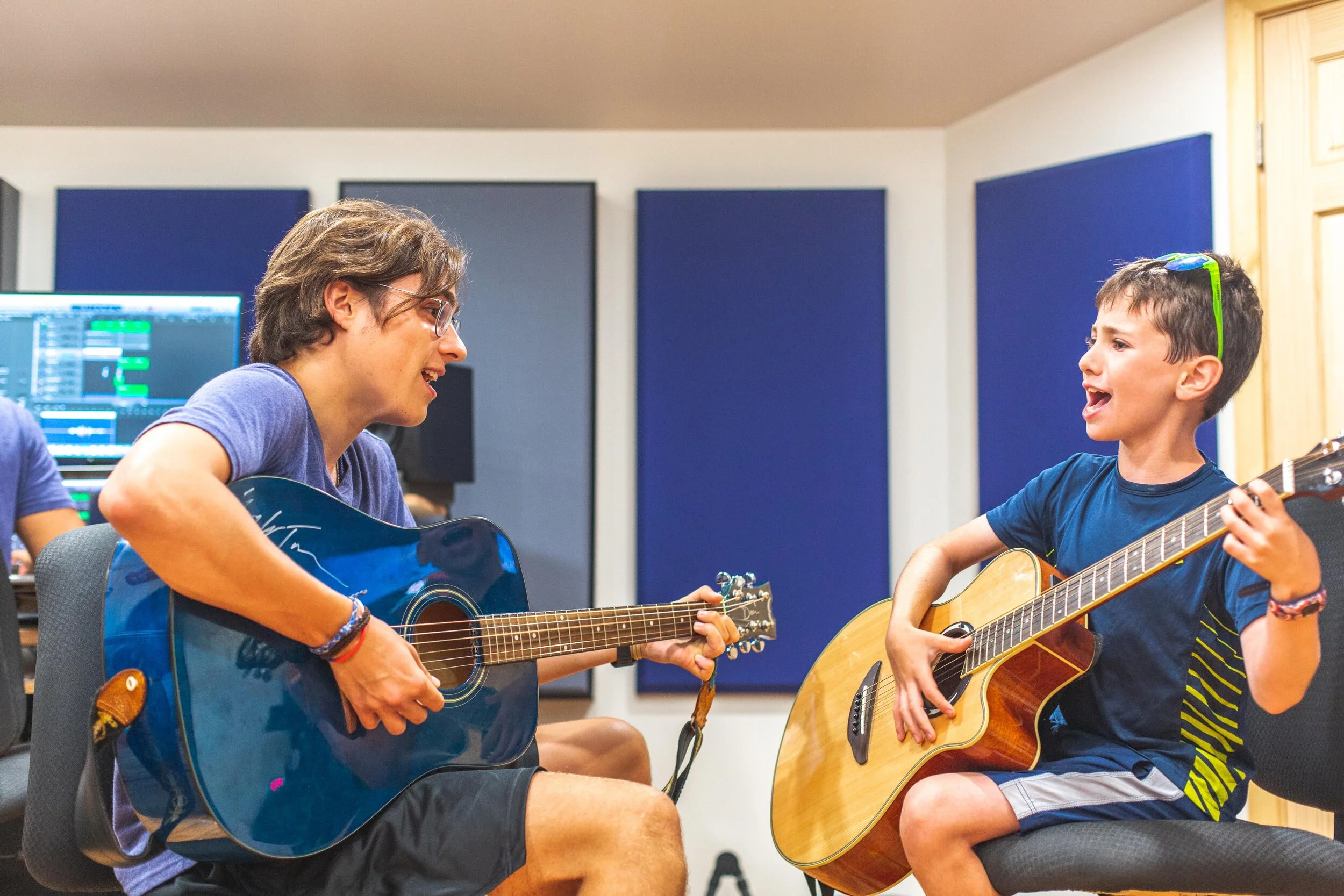 Two boys playing guitars and singing together in a music studio.