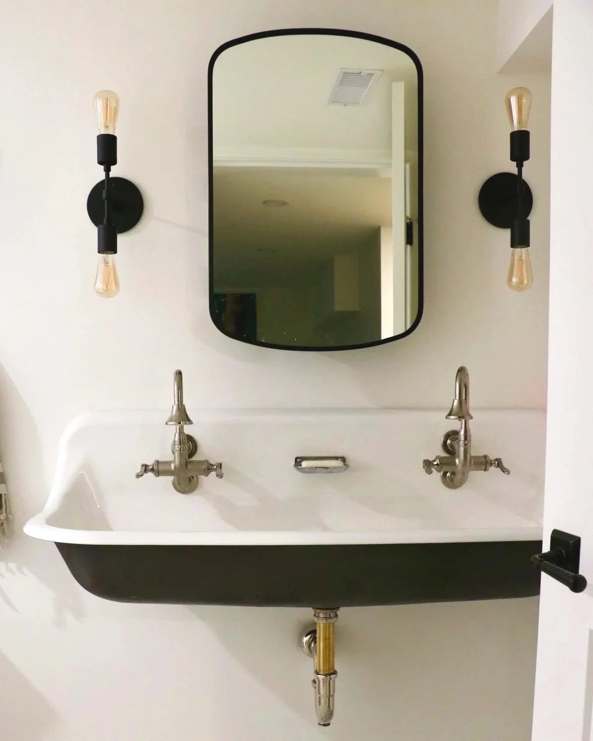 Modern-Vintage flare for bathroom double sink with two faucets, a mirror above, and two wall sconces with exposed bulbs to capture the mid-century essence.