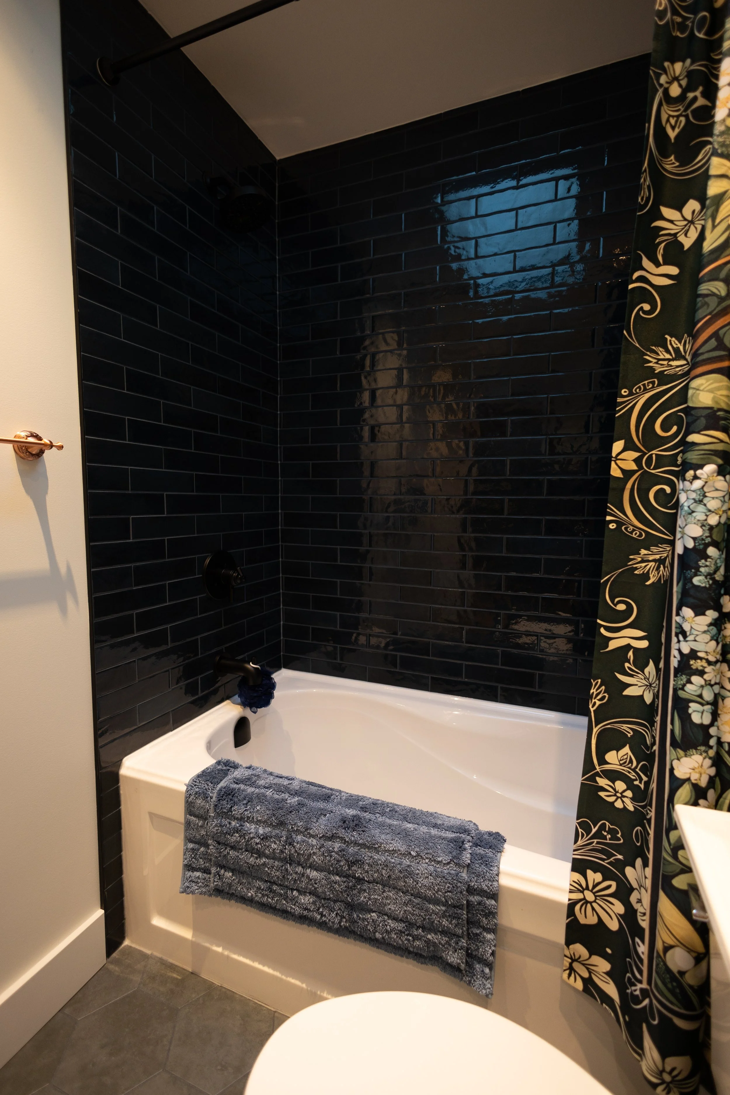 Updated bathroom with moody black-green subway tile that changes in the light and black plumbing fixtures. 