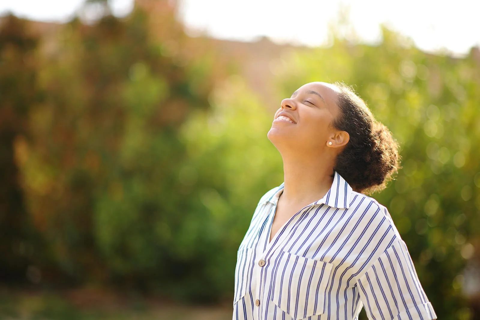 A smiling woman stands outdoors with her eyes closed and face lifted toward the sky. This moment of embodied calm reflects what becomes possible through EMDR therapy in Saint Paul, MN or IFS therapy in St. Paul, MN.