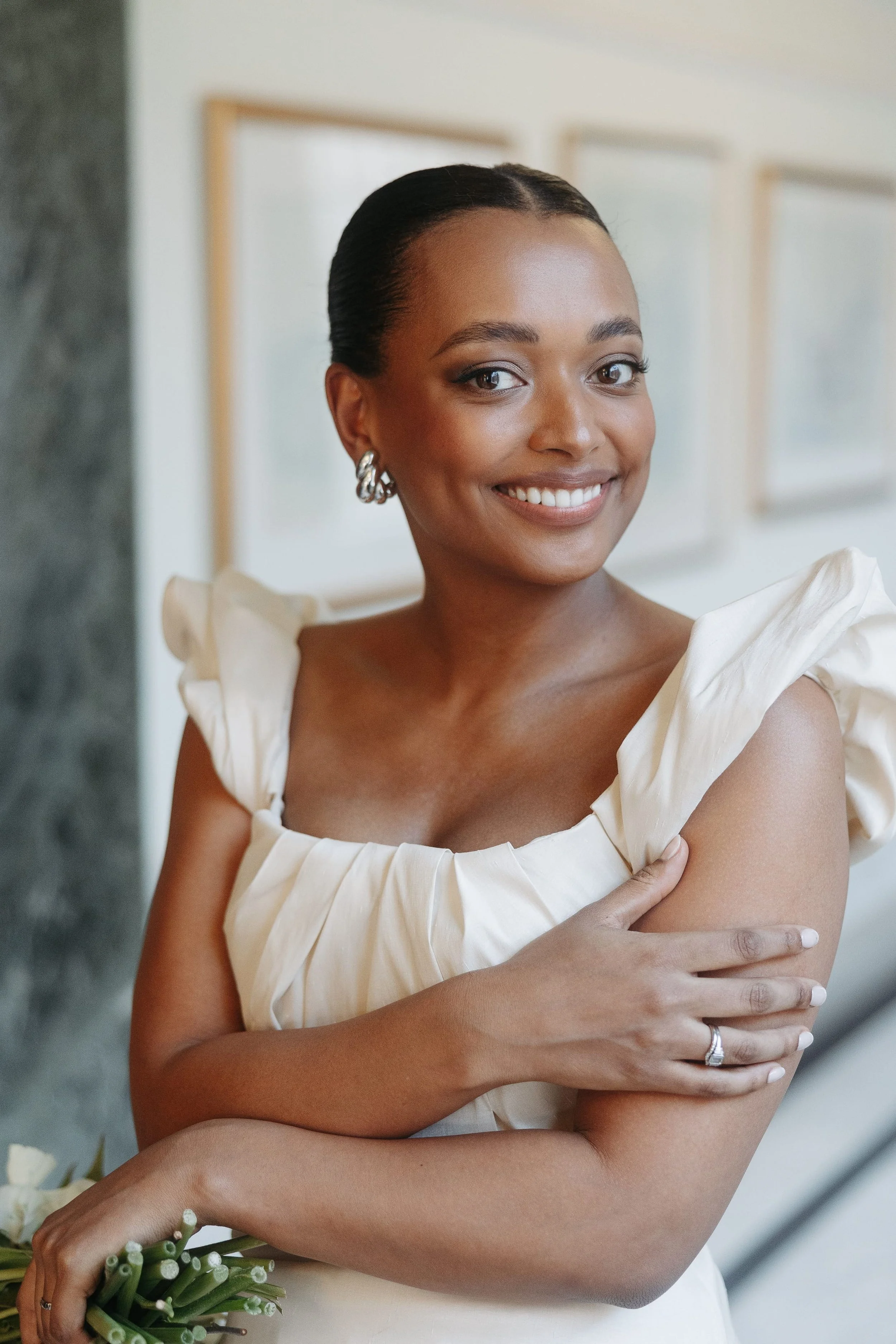 Bride on her wedding day, smiling at the camera. She wears natural wedding makeup and a simple, elegant updo.
