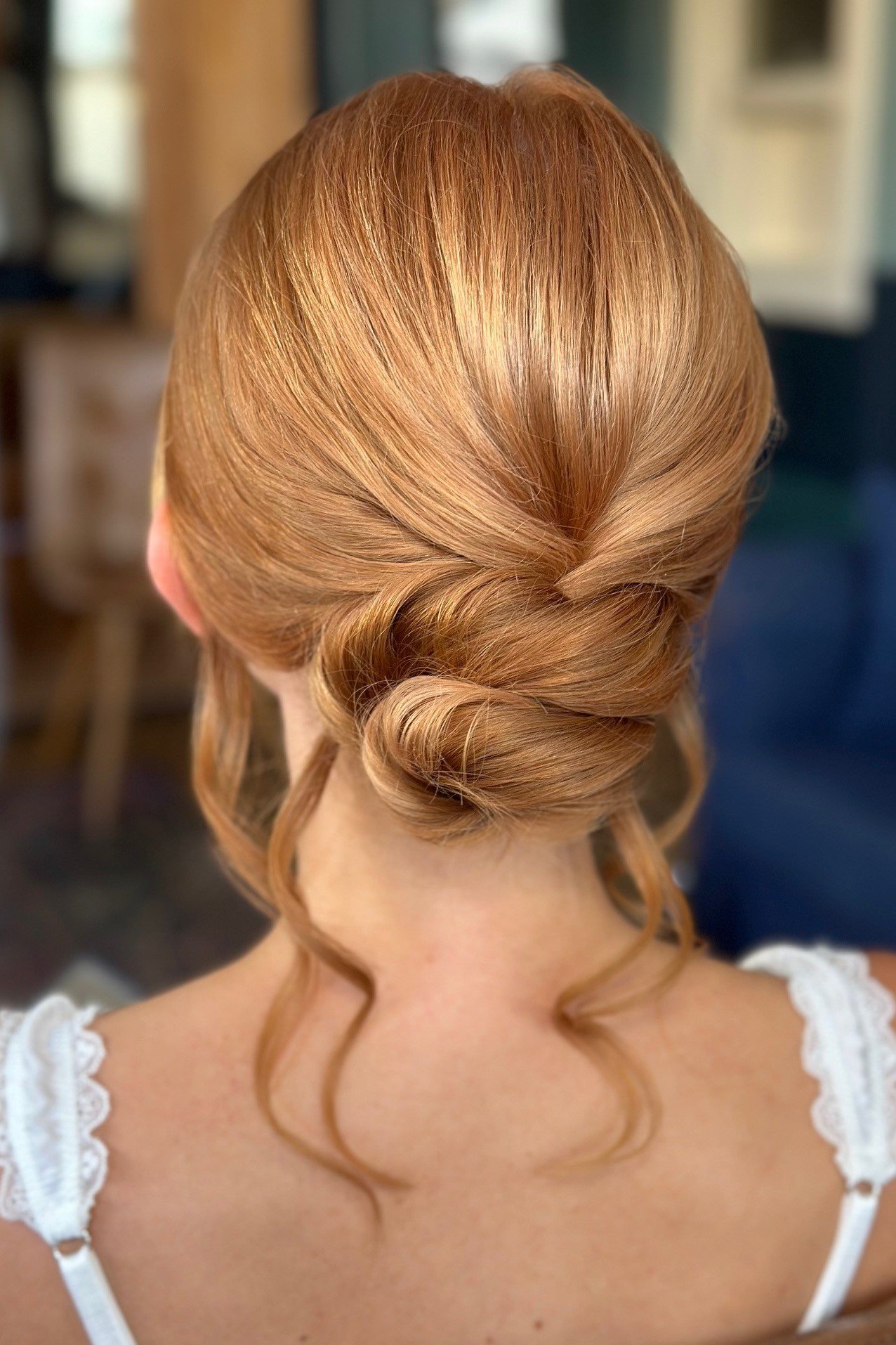 Back view of a woman with red hair styled in an elegant, textured updo with soft tendrils.