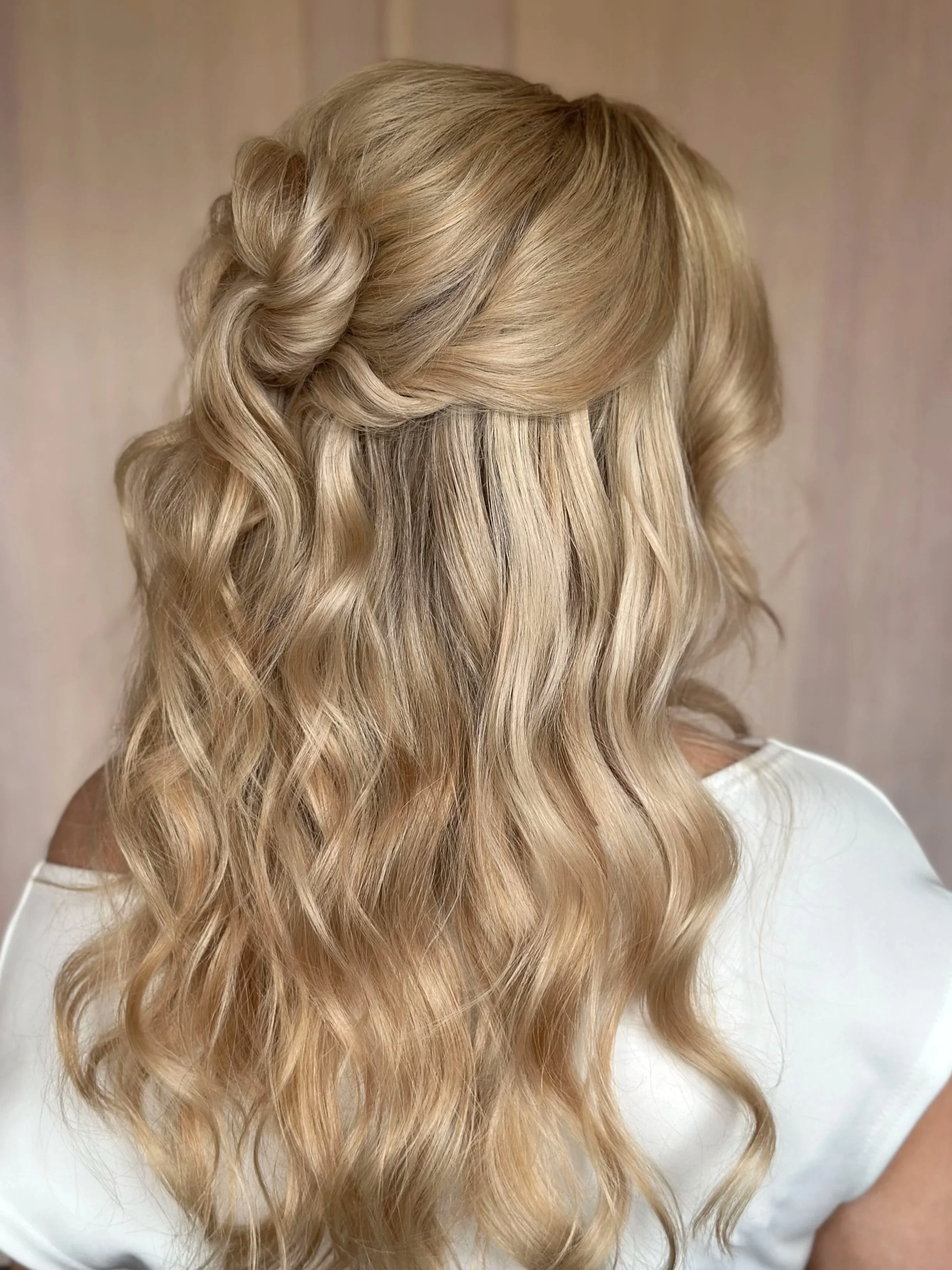 Back view of a woman's long, wavy blonde hair styled in loose curls with a side braid.