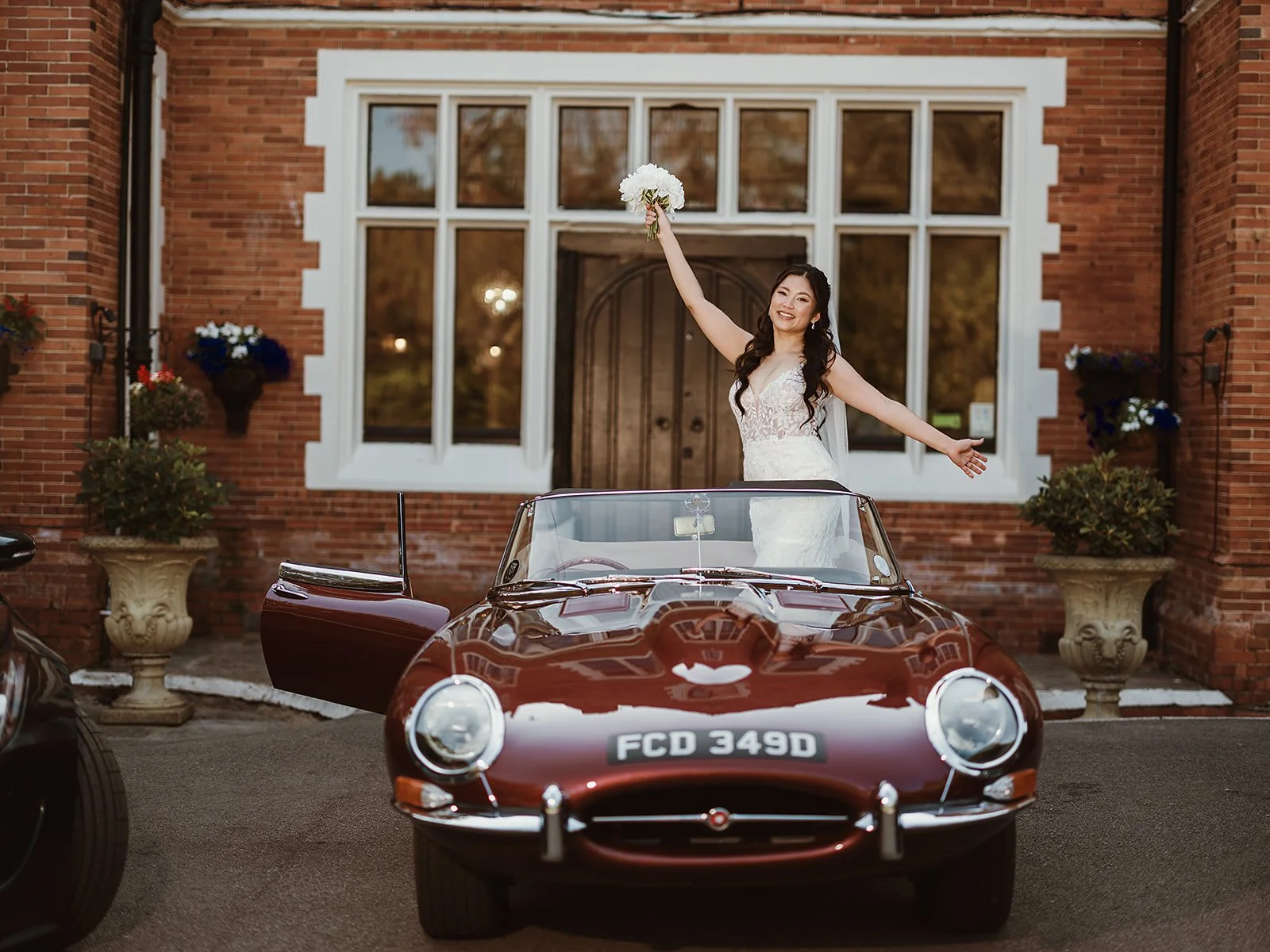 image of a bride standing in a vintage wedding car, holding her bouquet outside Highley Manor wedding venue